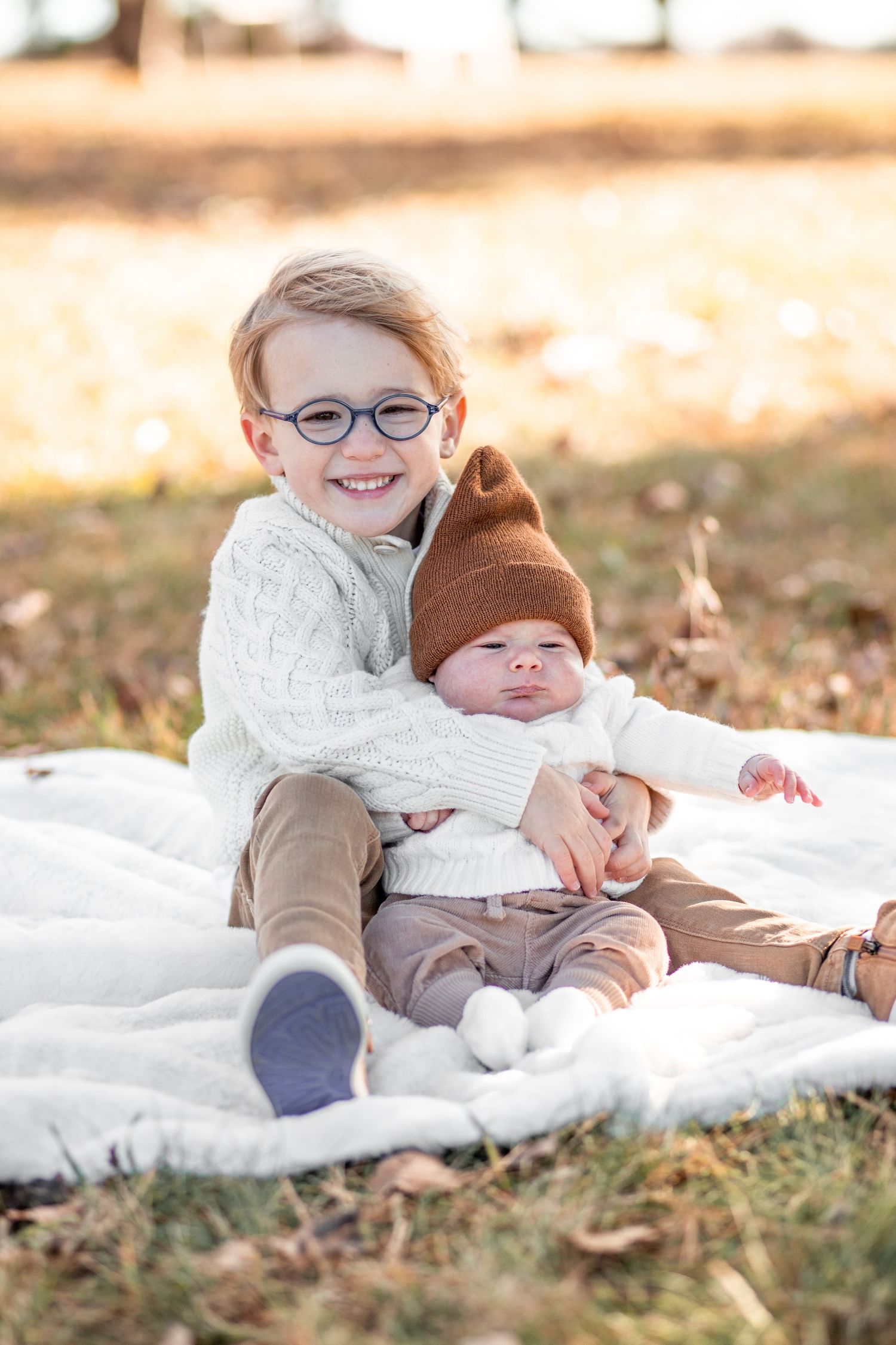 Two children lie on a blanket outdoors while sharing a sweet moment together during a fall photo session.