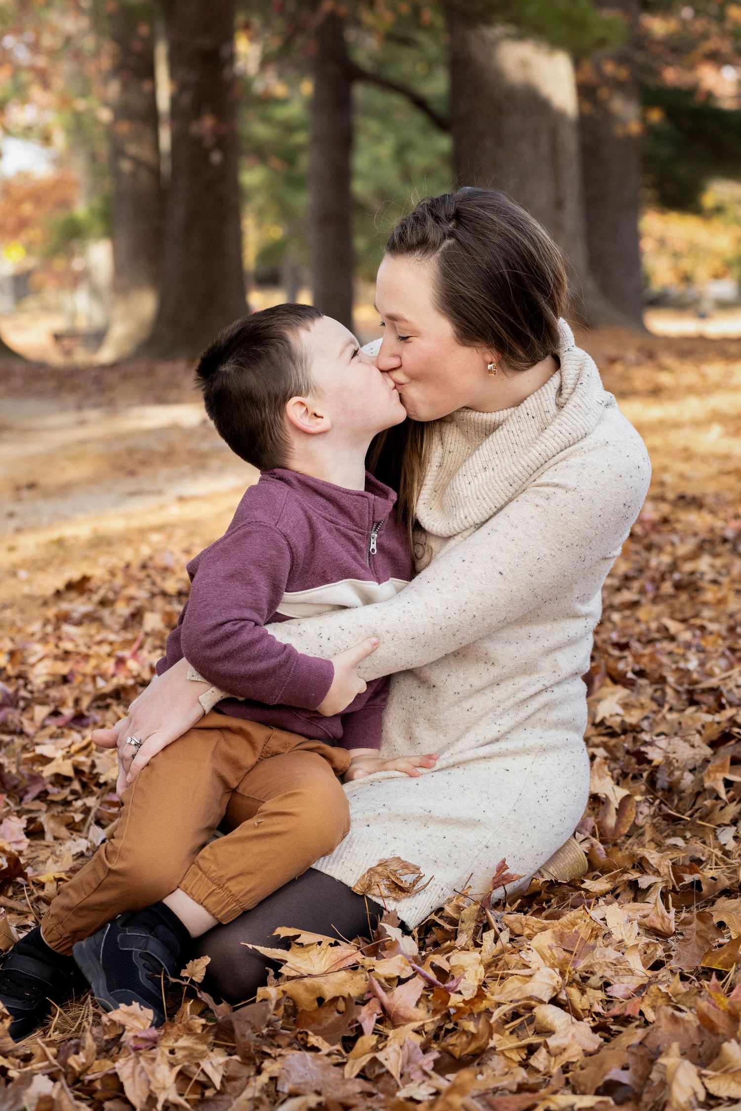 A tender moment captured between two people sitting among fallen autumn leaves in a park.