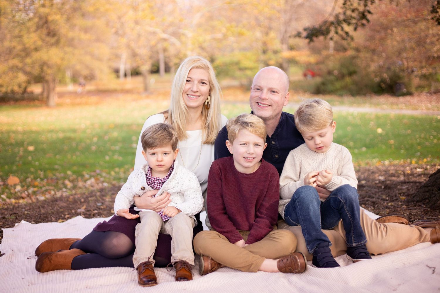 Children and adults relaxing together outdoors while posing for a series of casual family photos in an autumn setting.