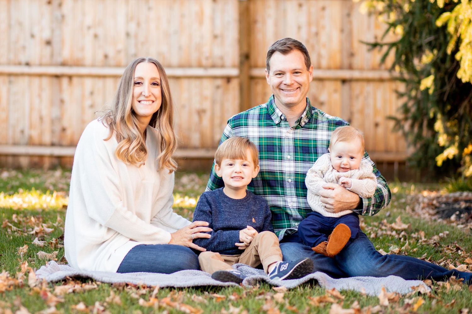 Family sitting together on blanket in backyard with wooden fence during autumn season.