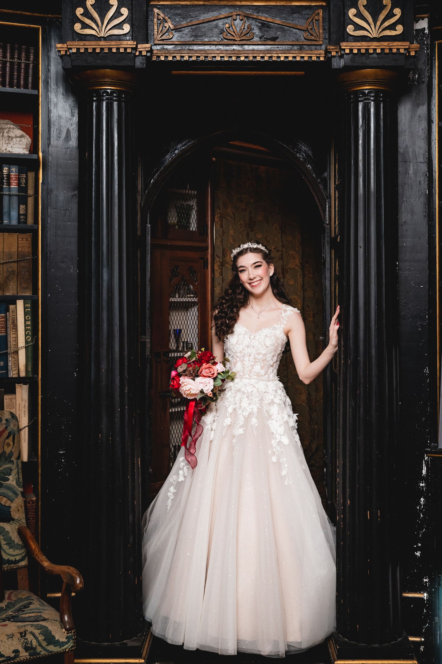 A person in an elegant white tulle ballgown poses against dark wooden architectural details in a vintage setting.