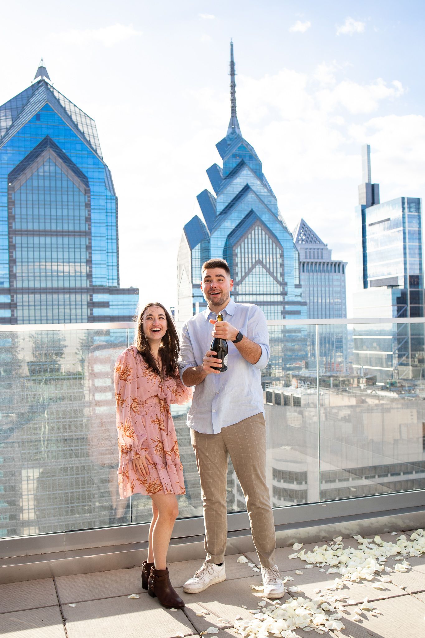 Two people enjoying drinks on a rooftop terrace with Philadelphia's iconic downtown skyline in the background.