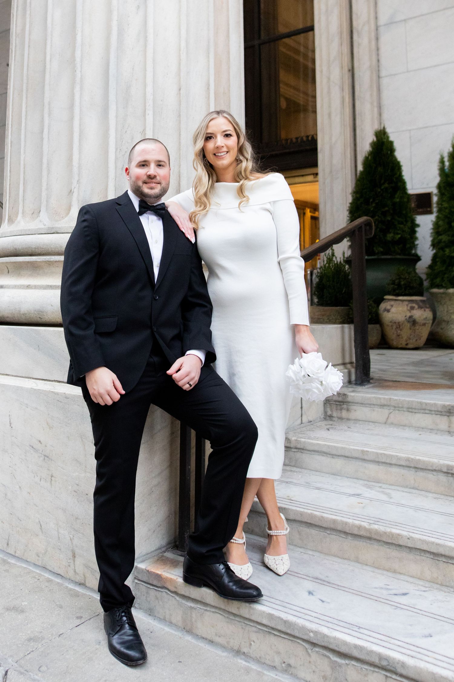 Couple posing on marble steps together while sitting and holding hands in formal attire.
