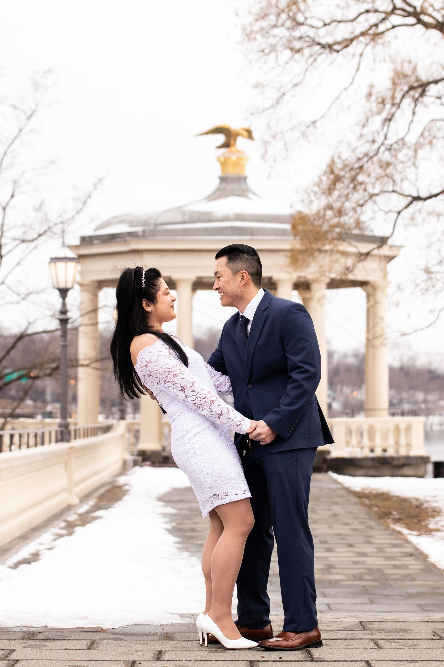 A couple in formal attire sharing romantic moments in front of stone architecture on a winter day.