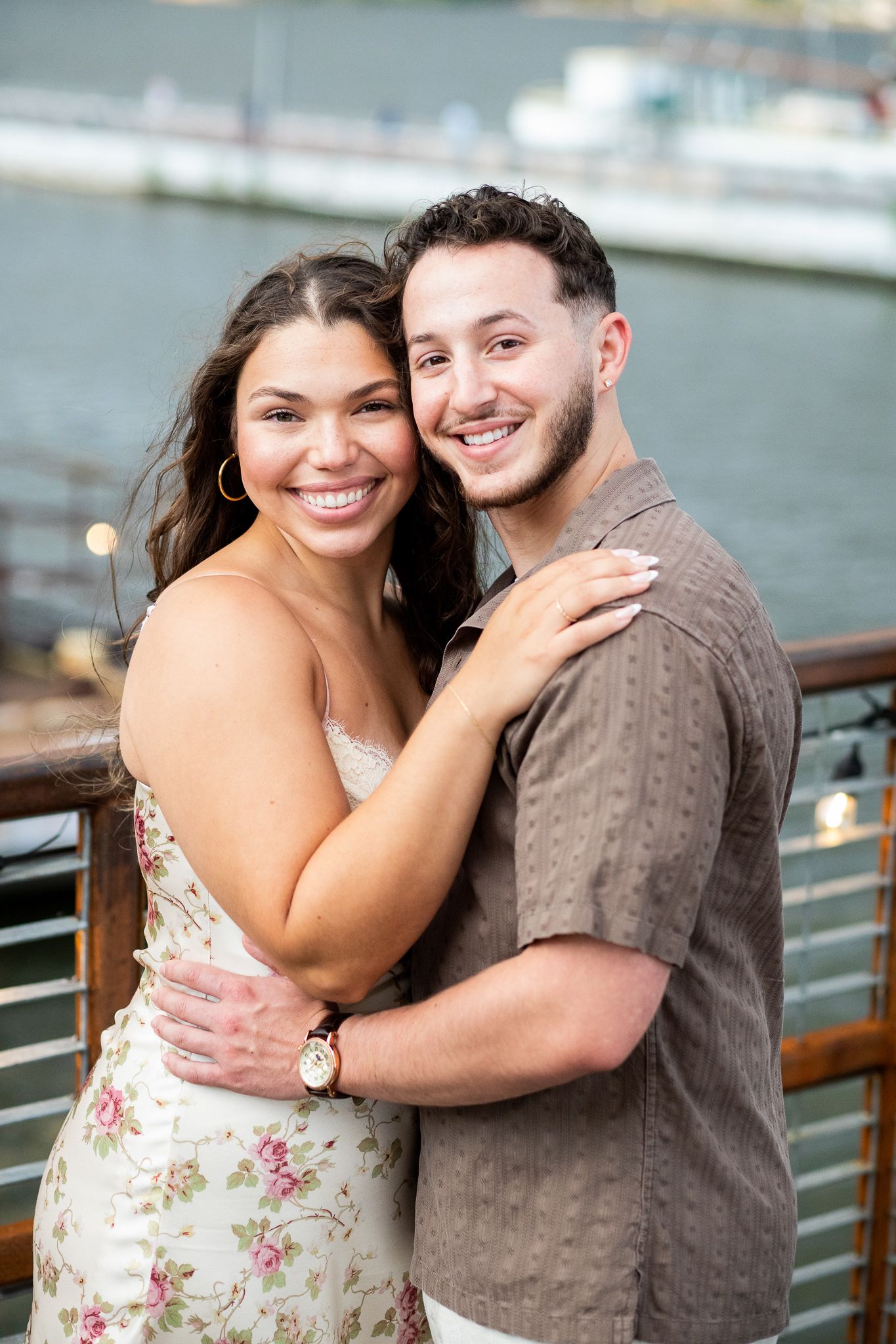 A couple embraces and smiles together during a romantic photoshoot by the waterfront.
