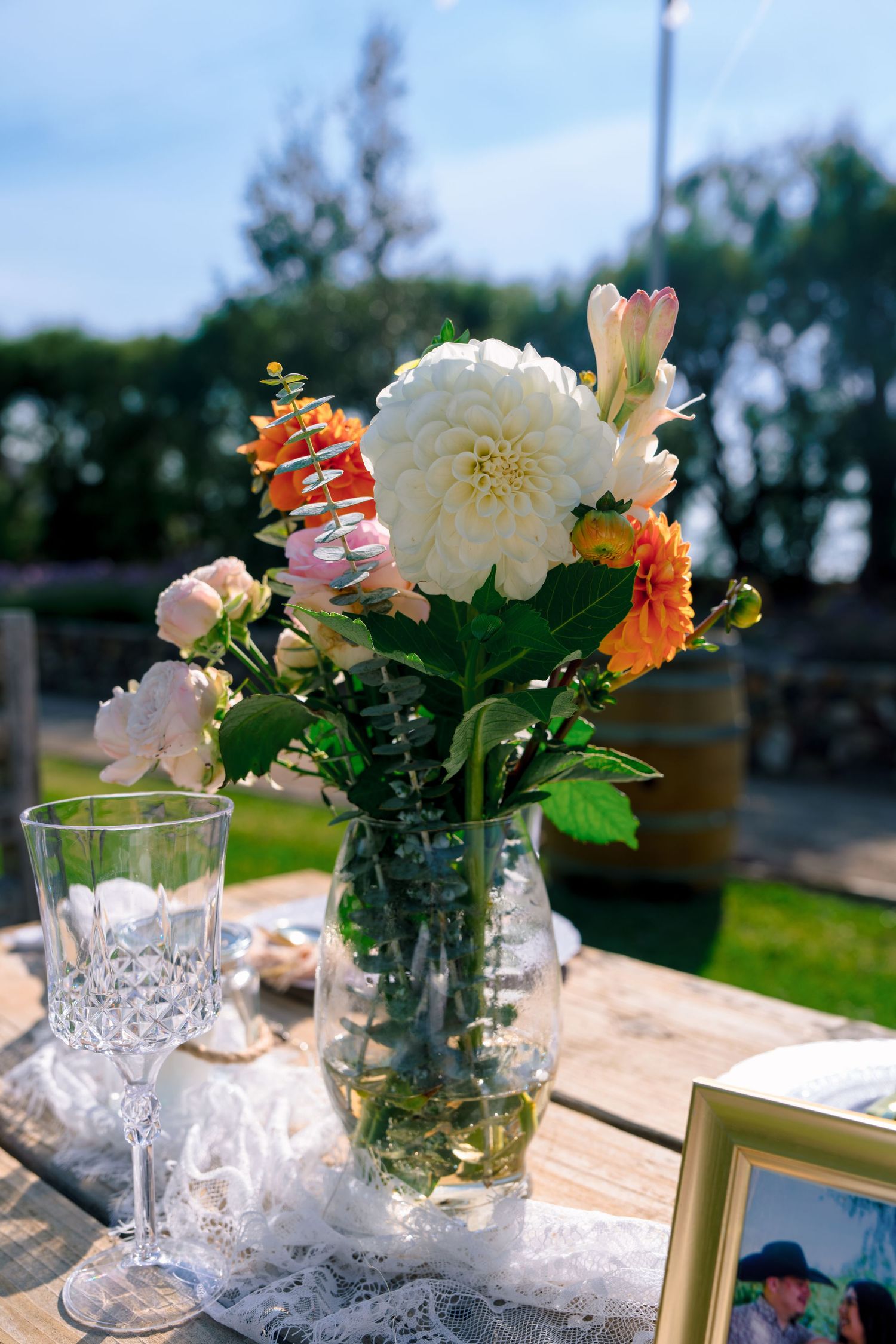 Elegant floral centerpieces with white and orange blooms in crystal vases on a lace tablecloth.