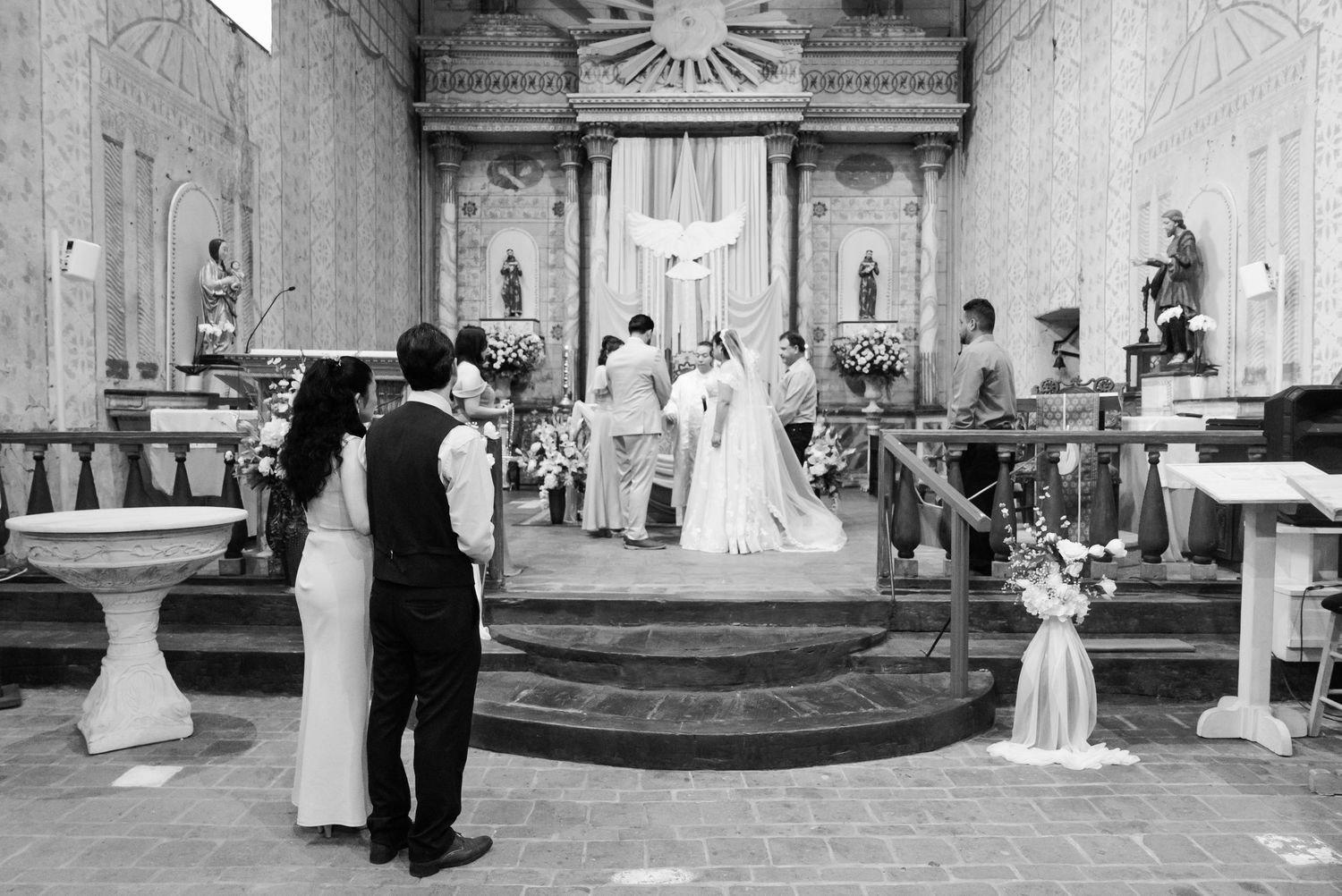 Black and white photograph of a traditional church wedding ceremony with ornate altar decorations.