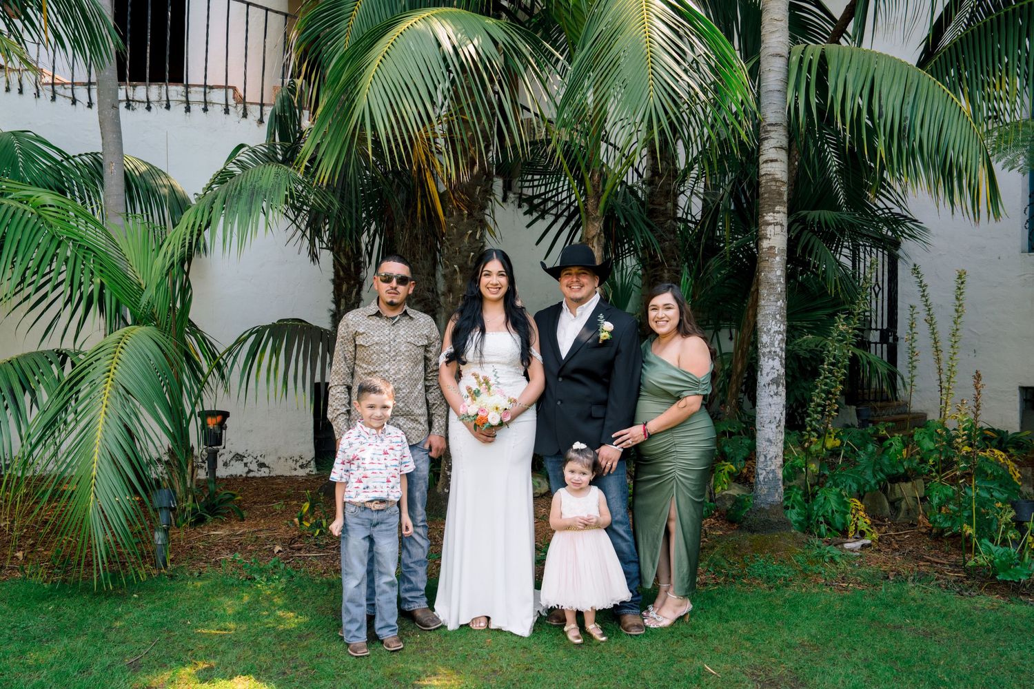 Wedding group poses for photos in a tropical garden setting.