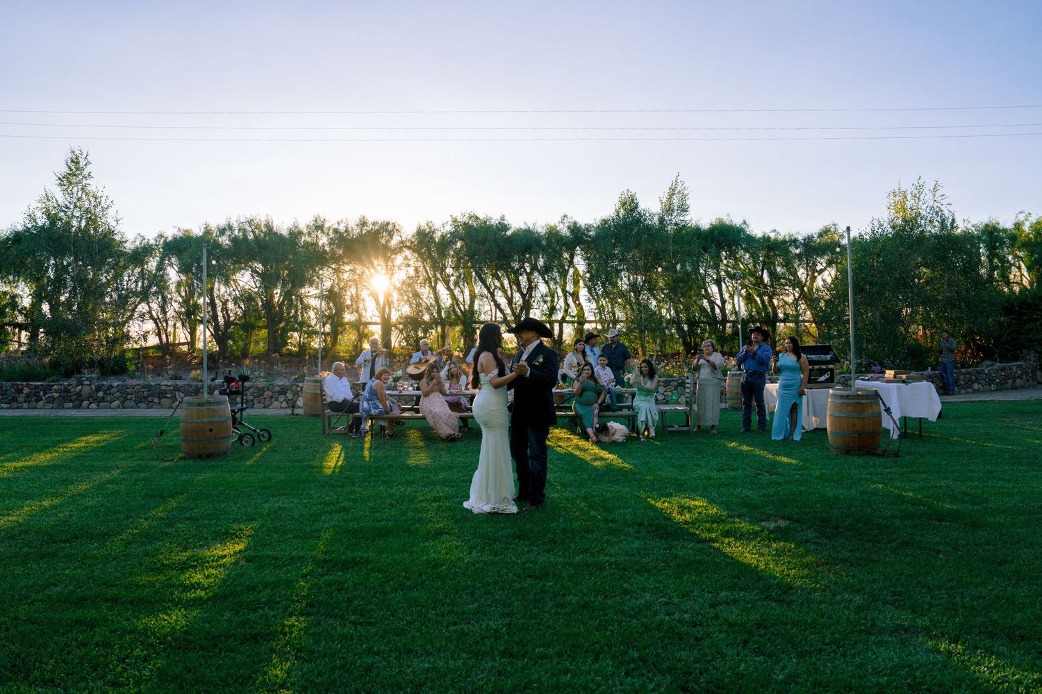An outdoor wedding reception on a lawn at sunset with guests mingling.