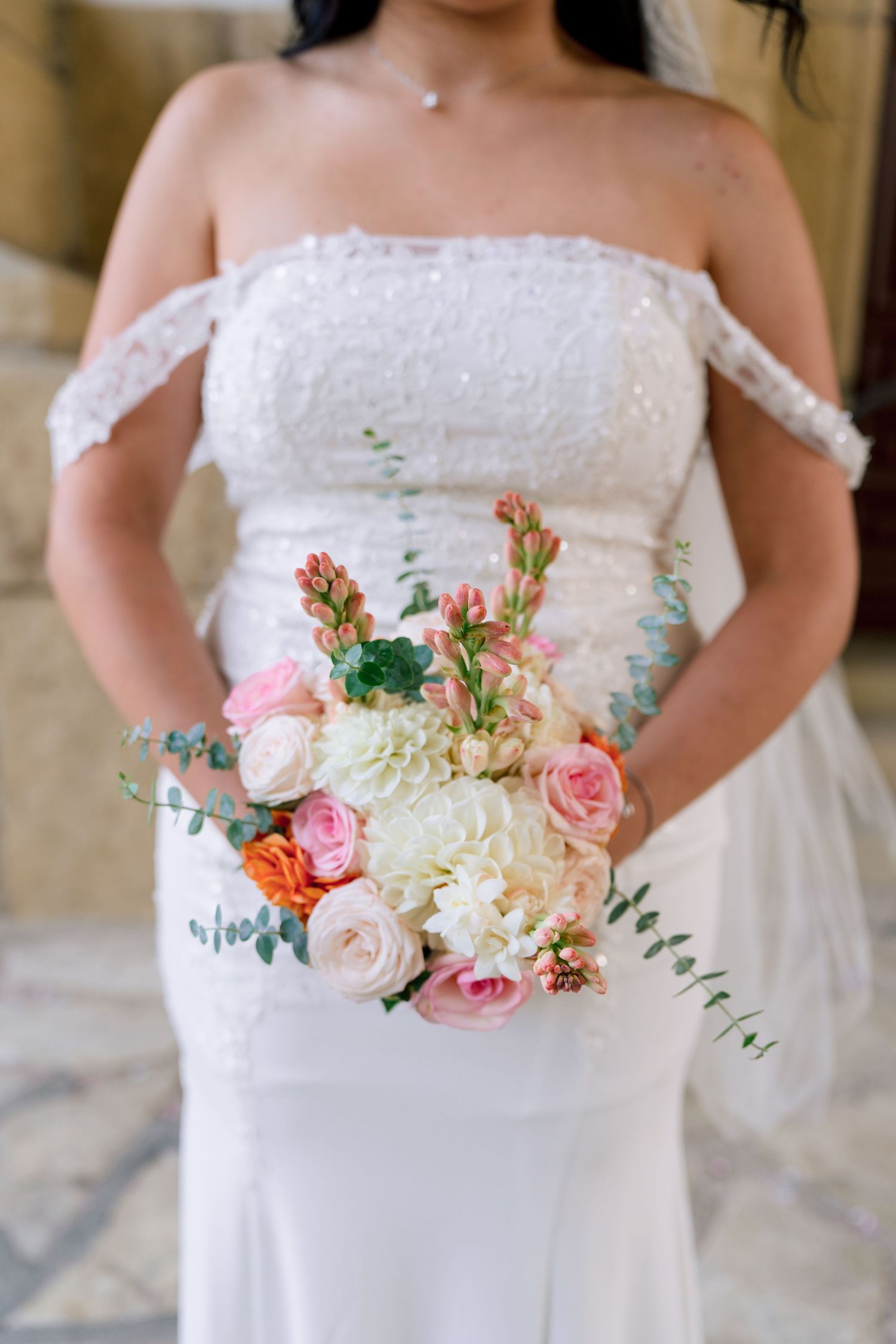 Bridal bouquet featuring pink roses, white flowers and eucalyptus against white wedding dress.
