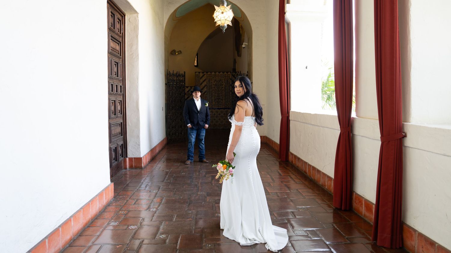 Long hallway with white walls, exposed wooden beams, and red curtains.
