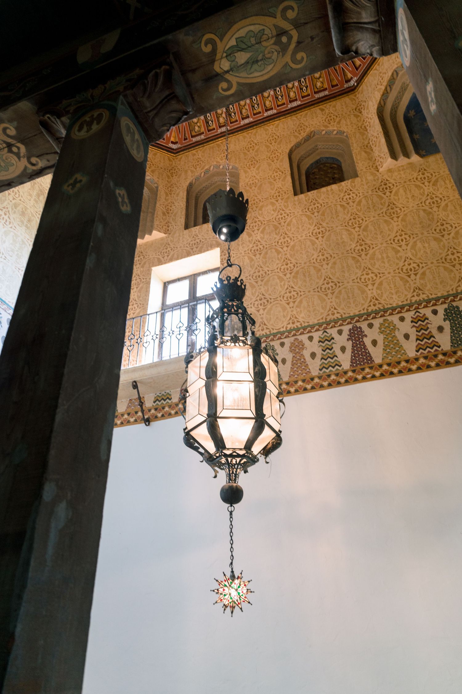 Ornate vintage chandeliers hanging from a decorative ceiling with detailed patterns.