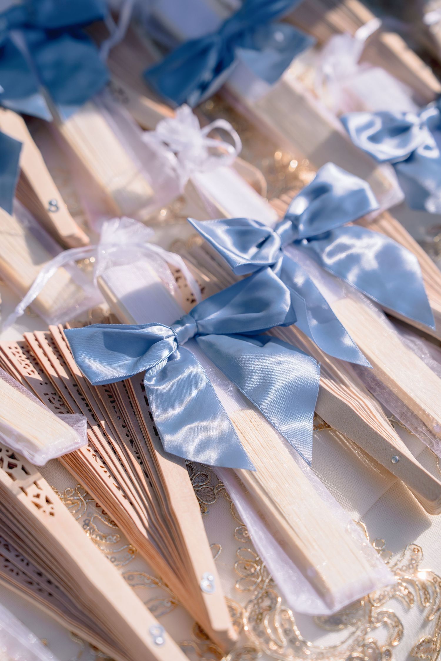 Wooden hand fans with blue satin ribbon bows displayed as wedding favors on a decorative tray.