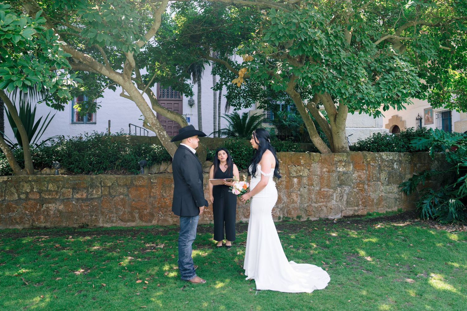 Wedding ceremony taking place in a lush garden setting with stone walls.