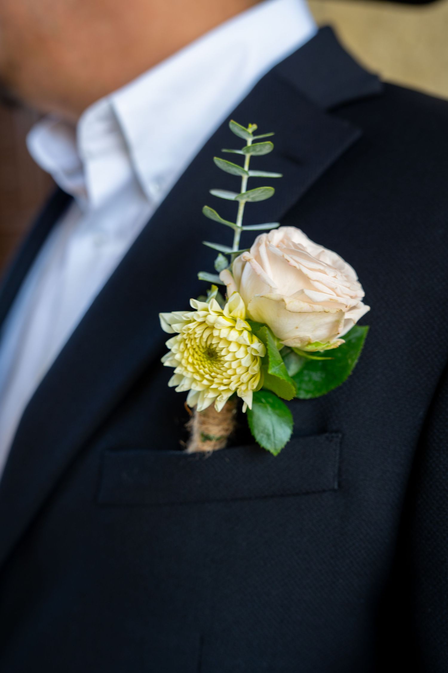 Elegant boutonniere with peach rose and greenery on black suit lapel.