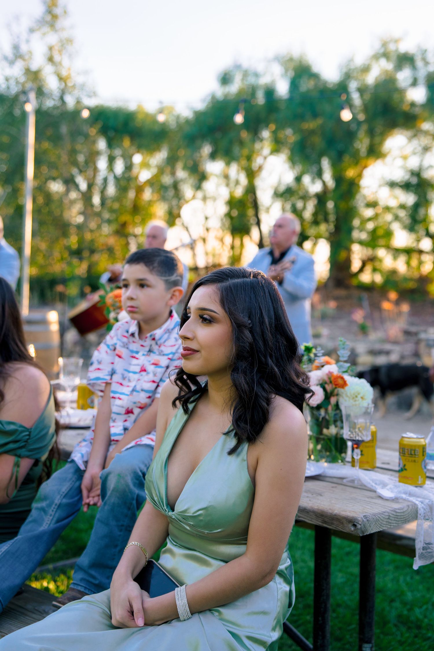 Wedding guests enjoy an outdoor reception with tables and sunset lighting.