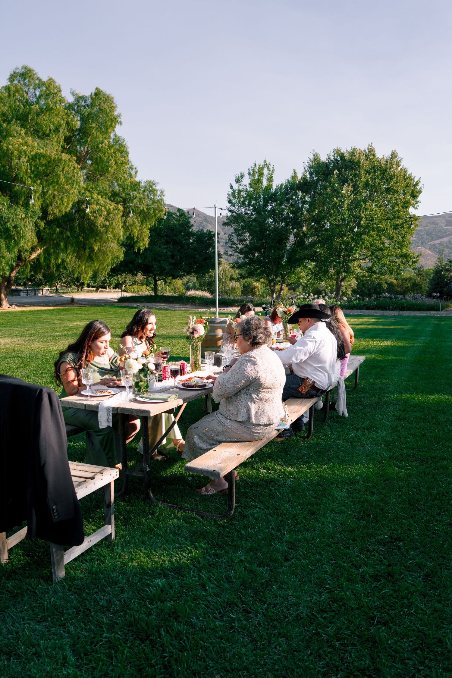 Wedding guests dine at picnic tables on a green lawn during outdoor reception.