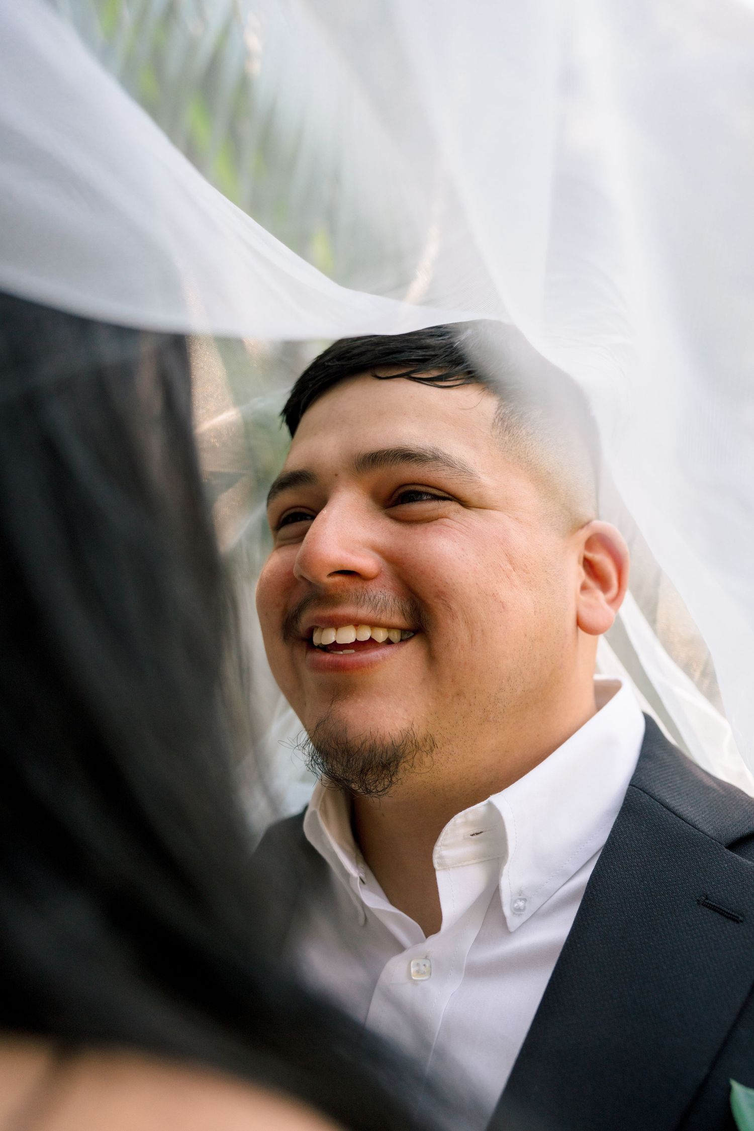 Close-up portrait showing joyful expressions and smiles through a white veil at a wedding.