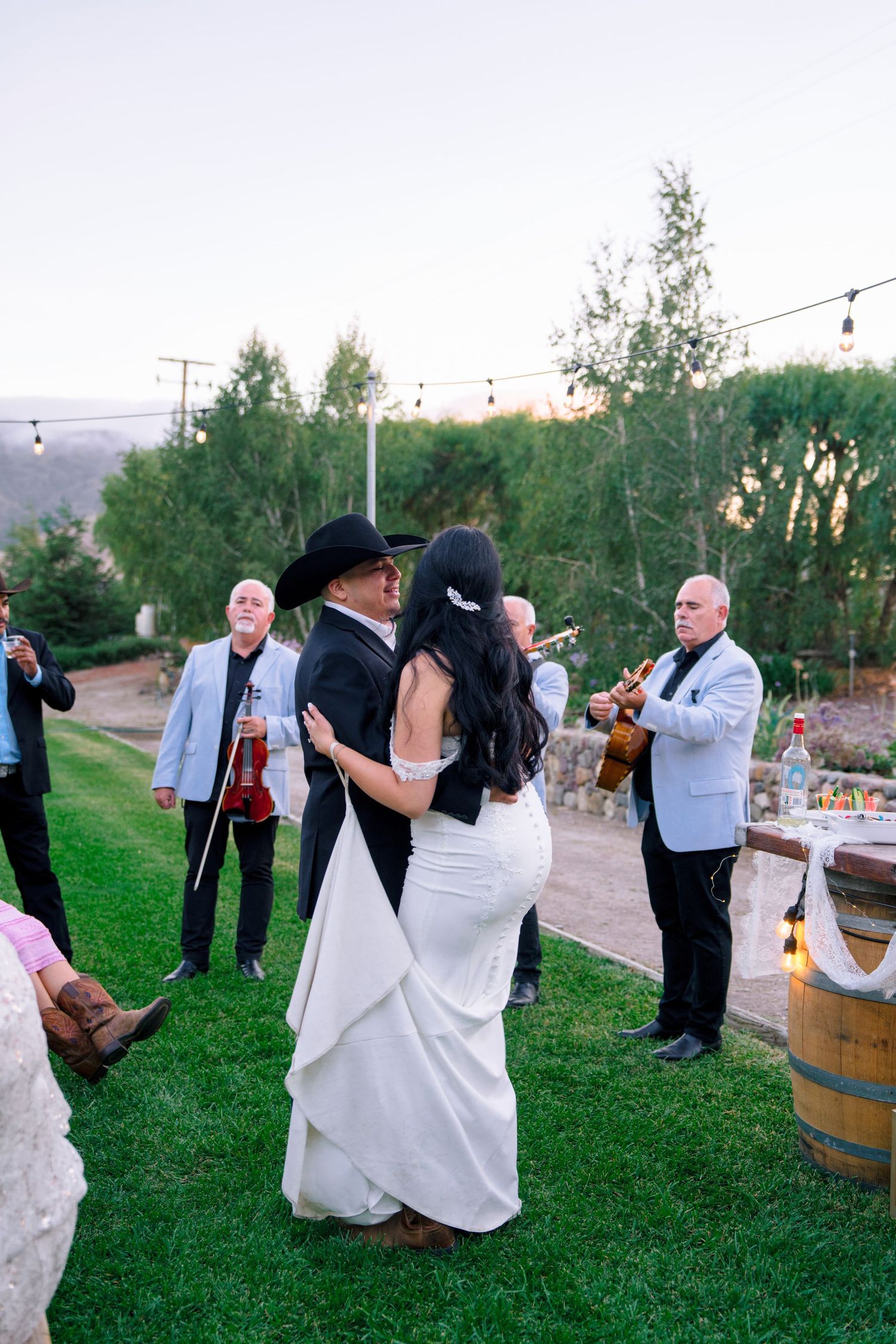 Wedding guests dancing and celebrating on a grassy outdoor venue at sunset.