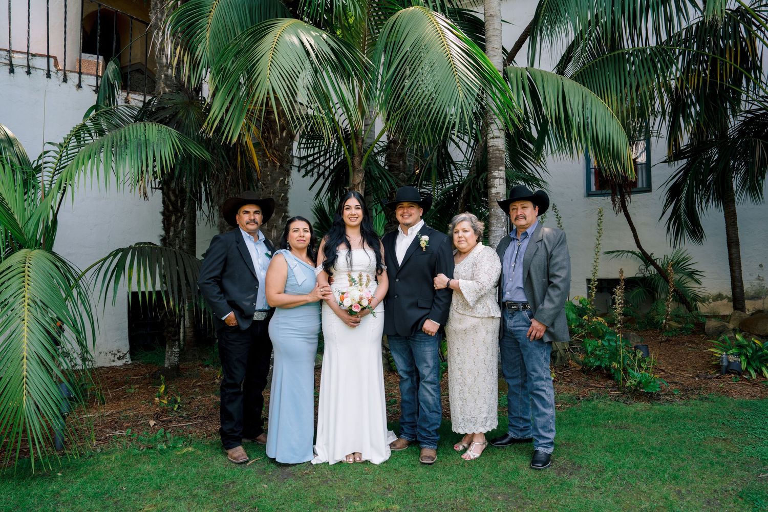 Wedding party members pose for group photos in a tropical garden setting.