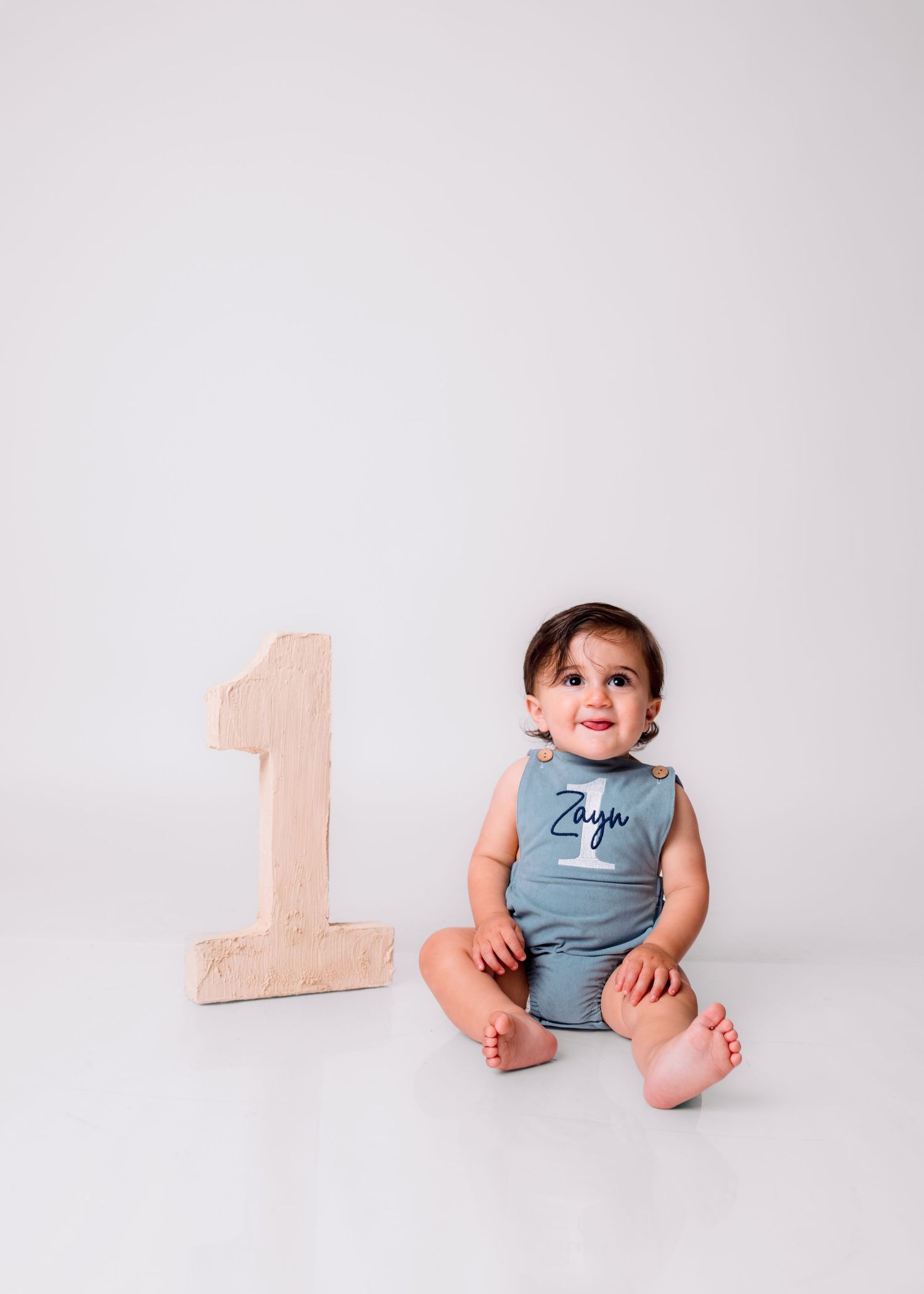 Cute baby boy named Zayn sitting beside wooden number one prop celebrating his first birthday.