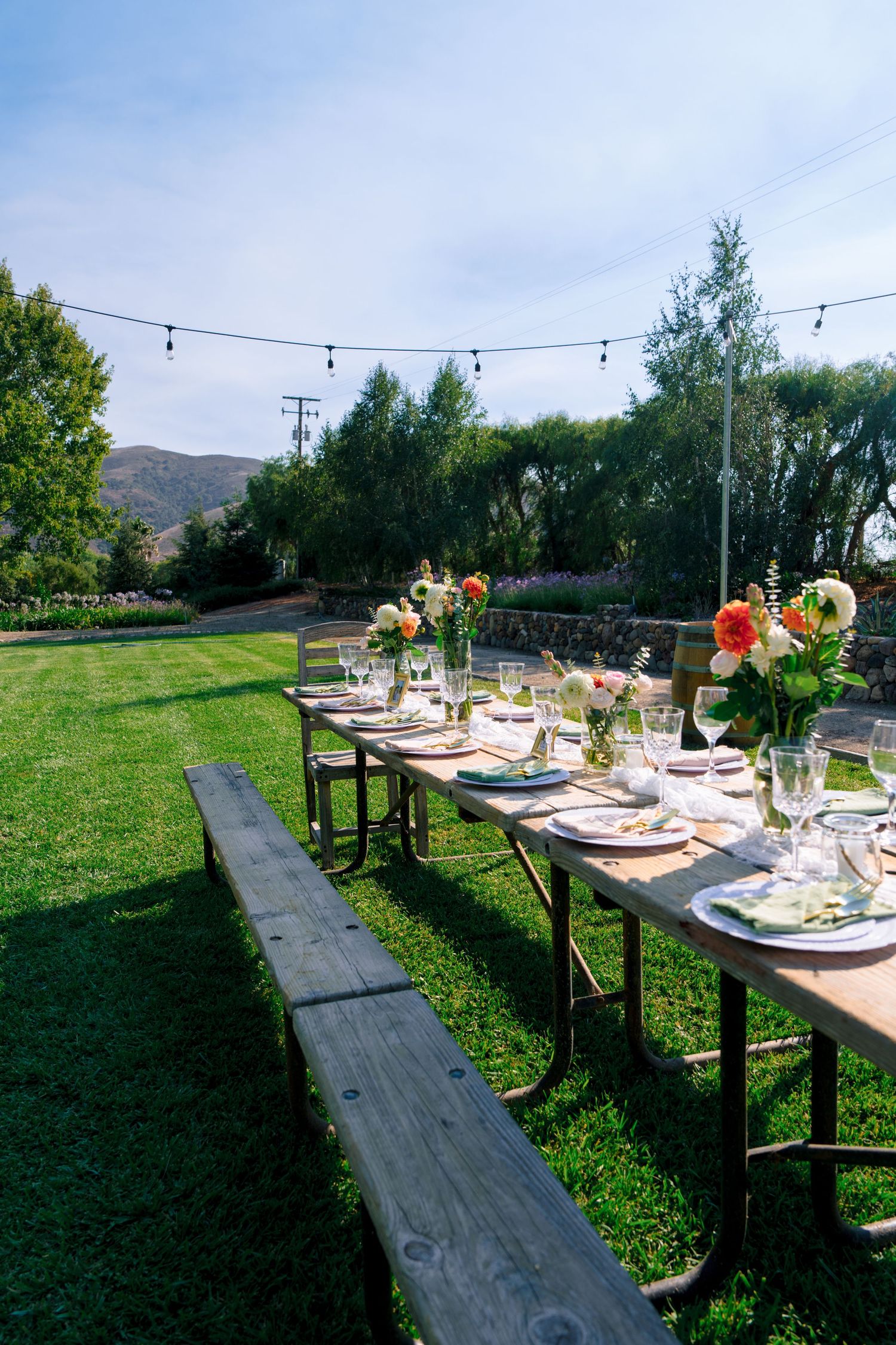 Long rustic dining tables with string lights and floral arrangements set against a mountain backdrop.