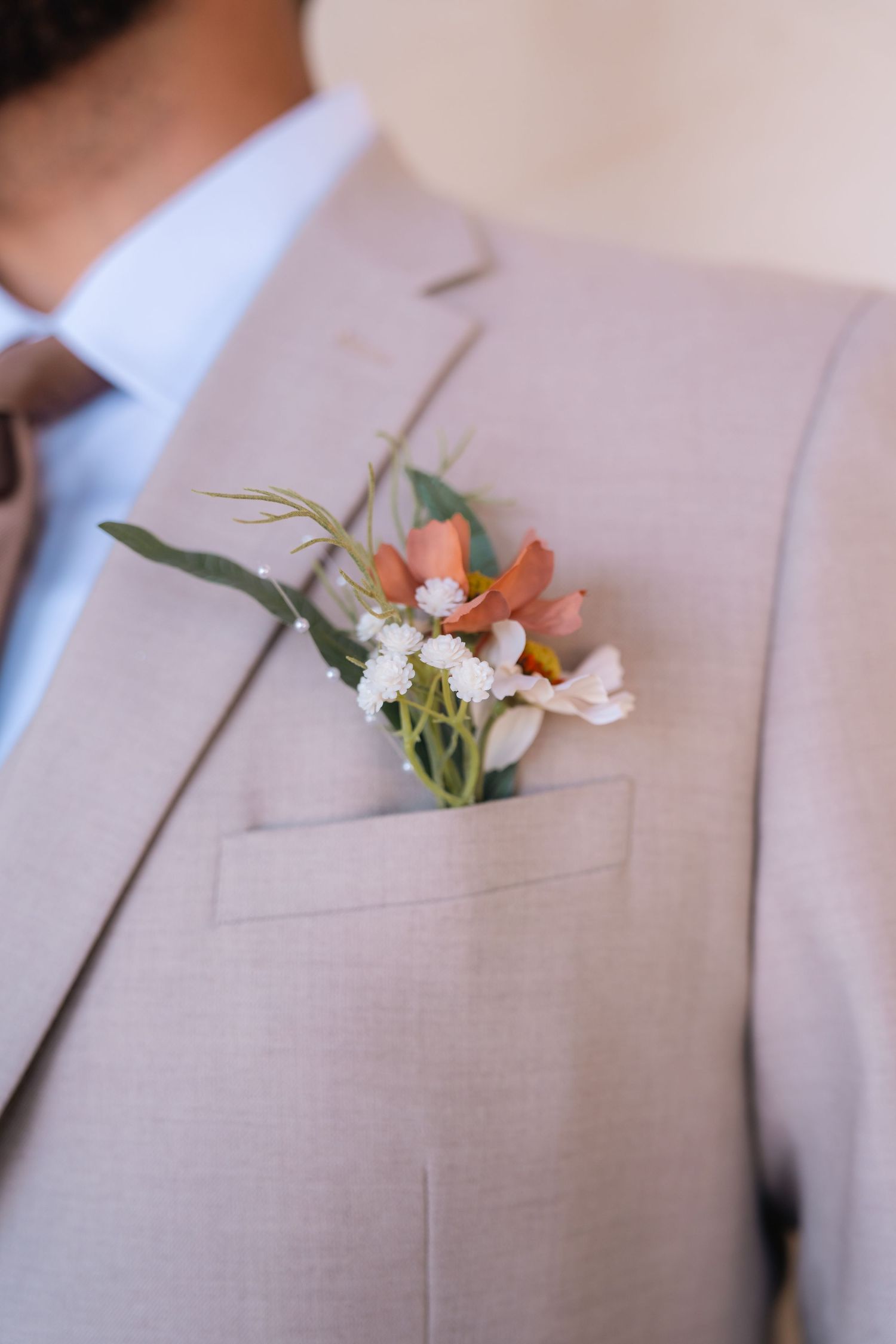 Delicate floral boutonniere with coral and white blooms pinned to a light gray suit jacket.