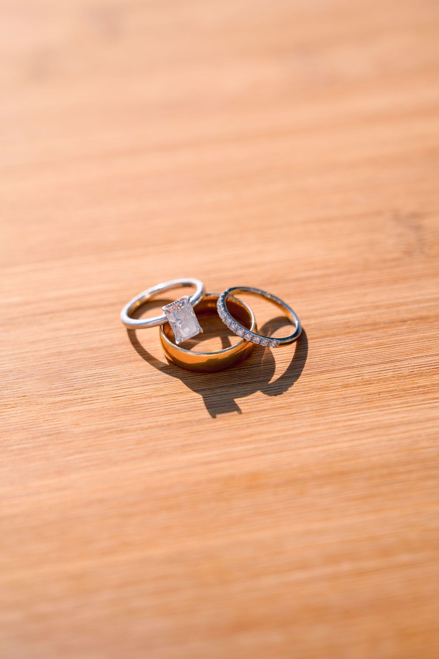 Two gold wedding rings casting shadows on a wooden surface in natural light.