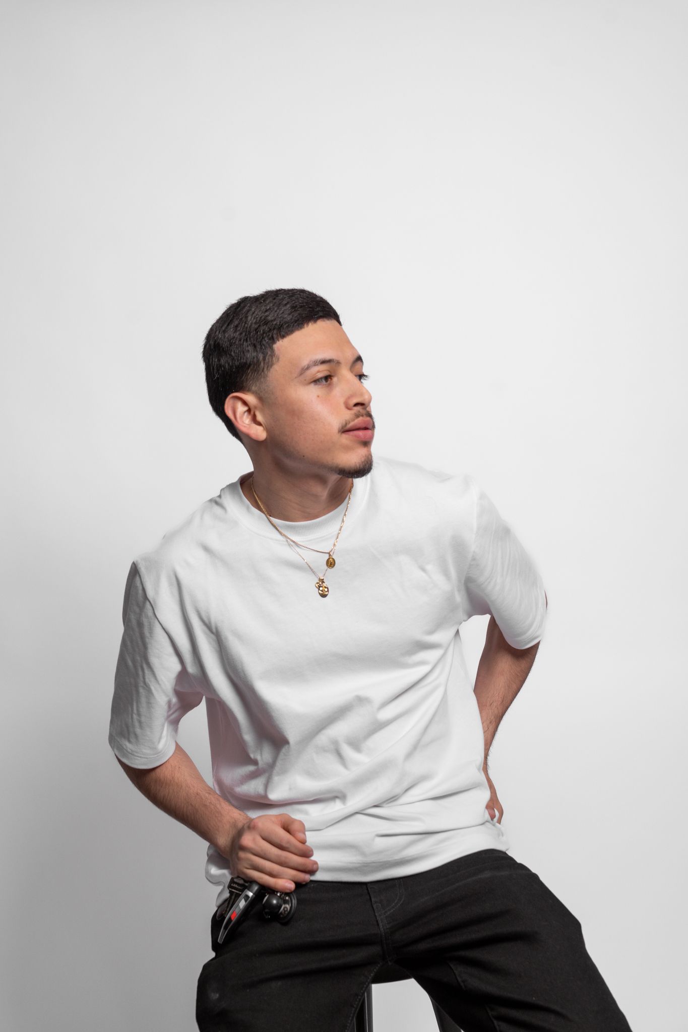 Model in white t-shirt and black pants poses against white background looking to the side.