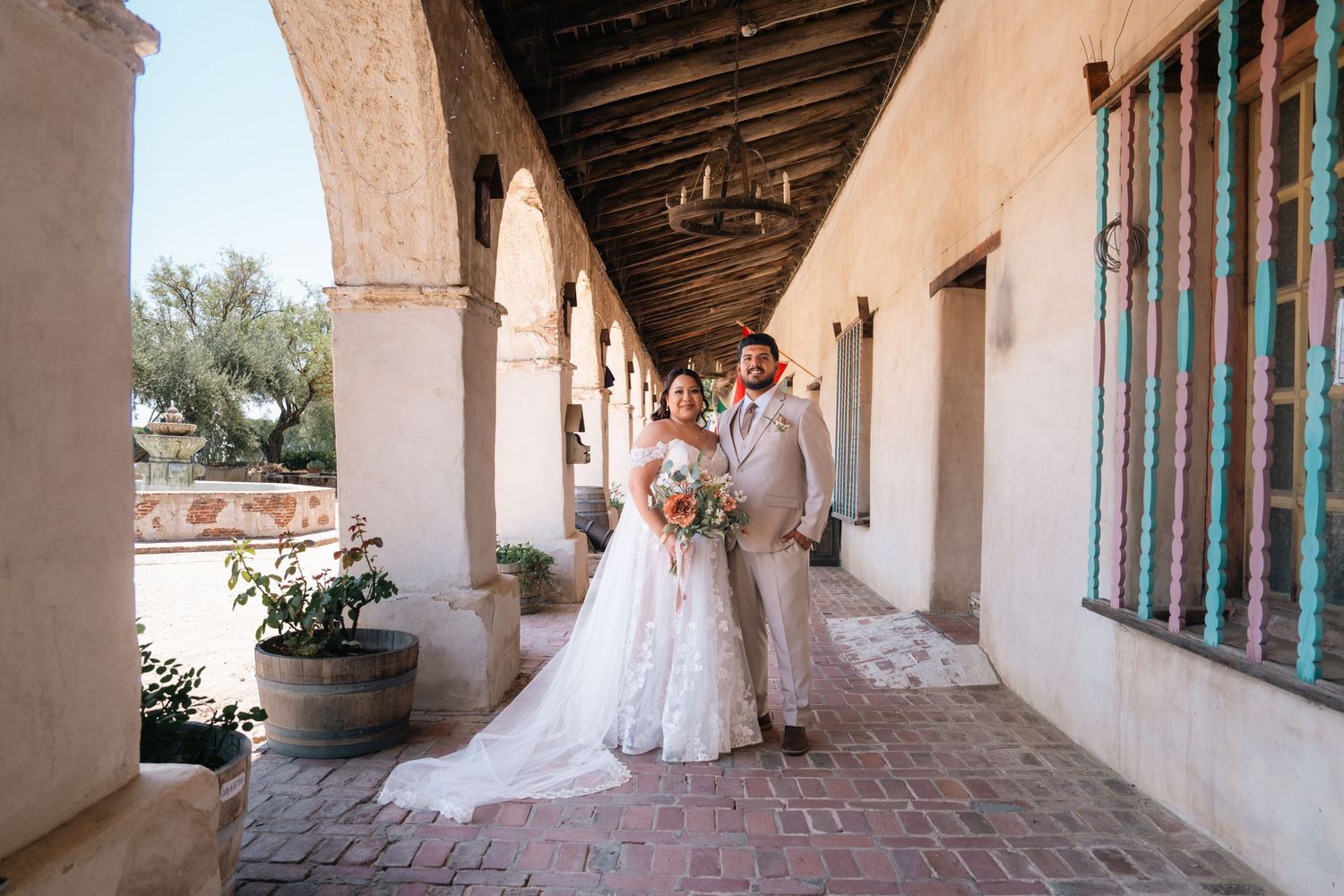 Bride walking through Spanish colonial style covered walkway with arched windows.