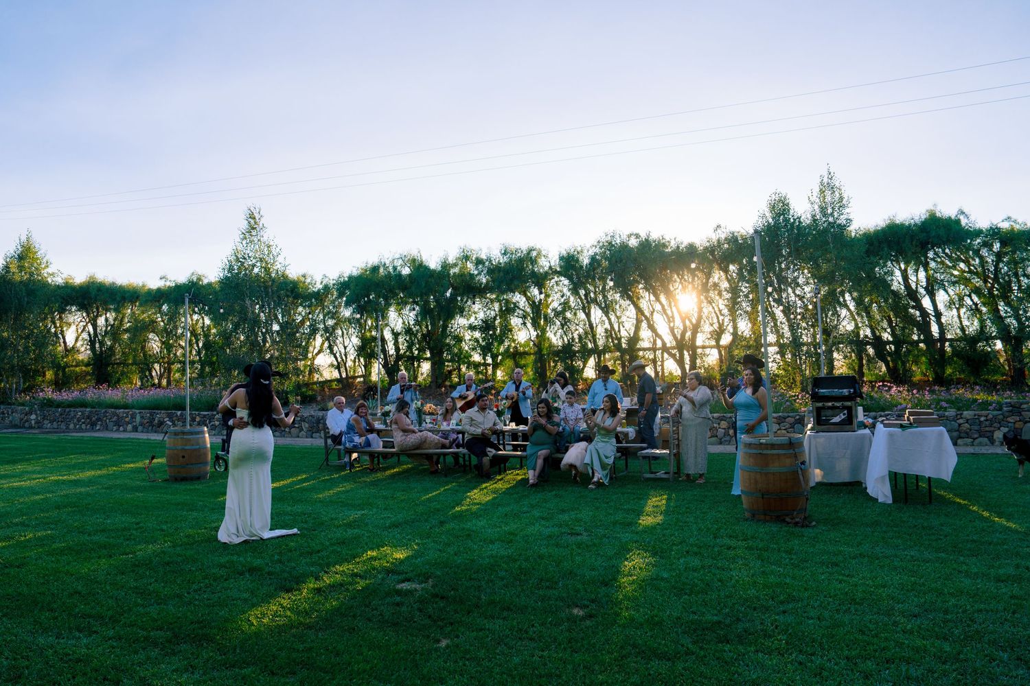 Wedding guests gather at outdoor tables during sunset reception.