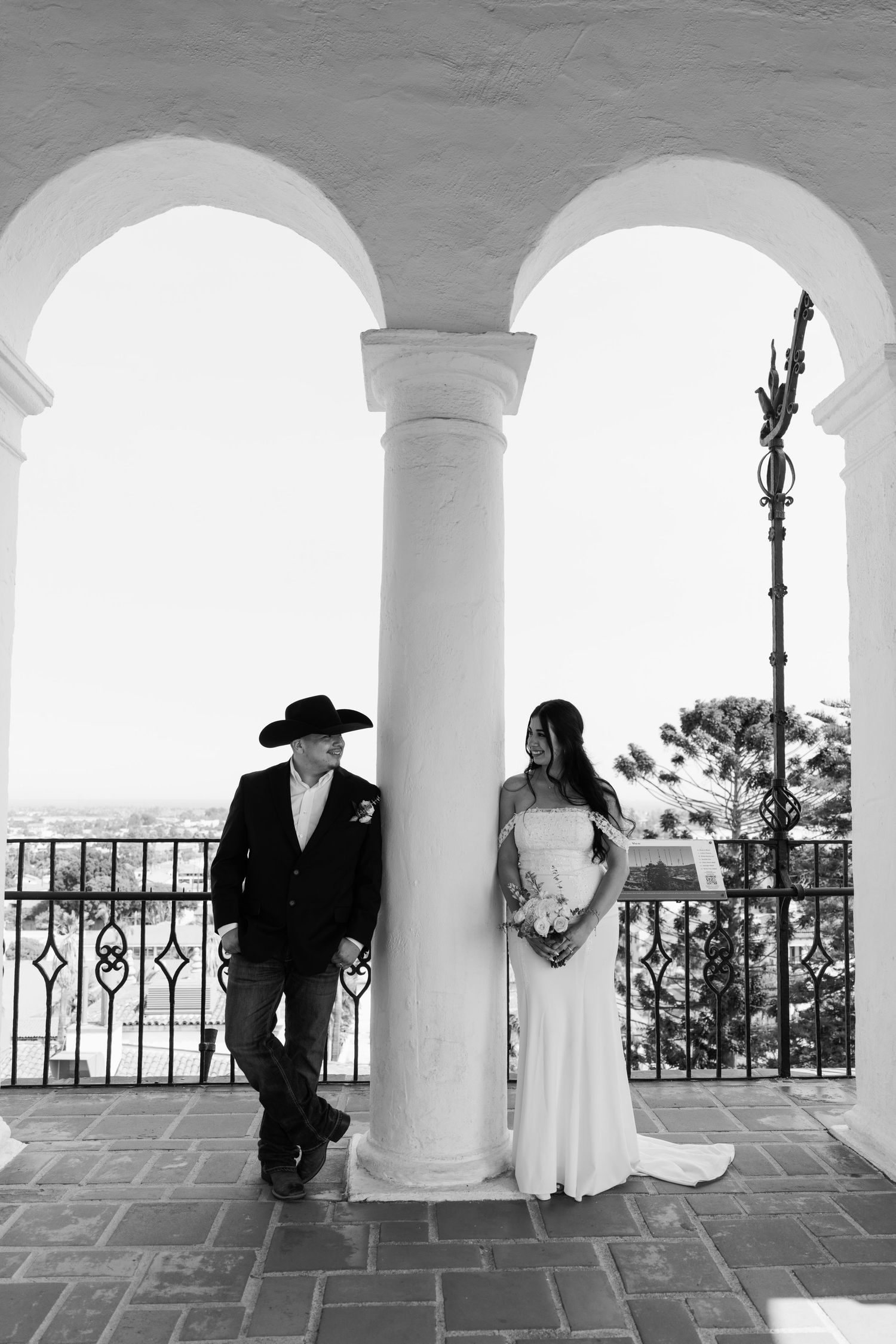 Black and white photo of a couple under arched columns overlooking a scenic view.