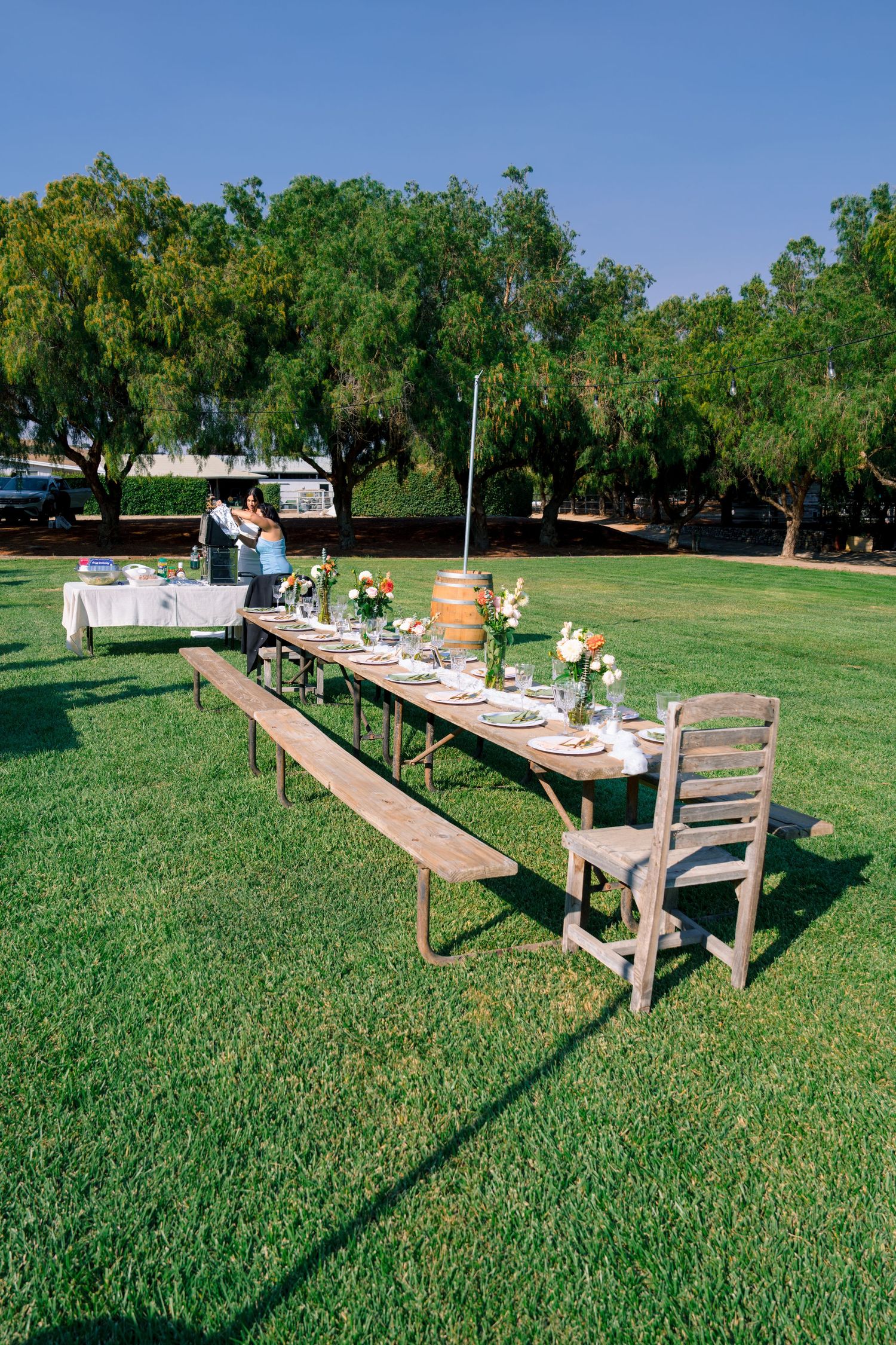 Long wooden dining tables with benches set up on a green lawn for an outdoor event.