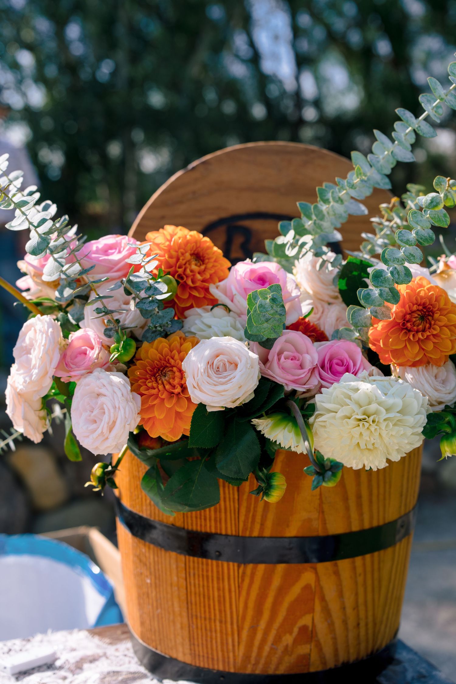 Beautiful floral arrangement with pink roses and orange dahlias in a wooden barrel container.