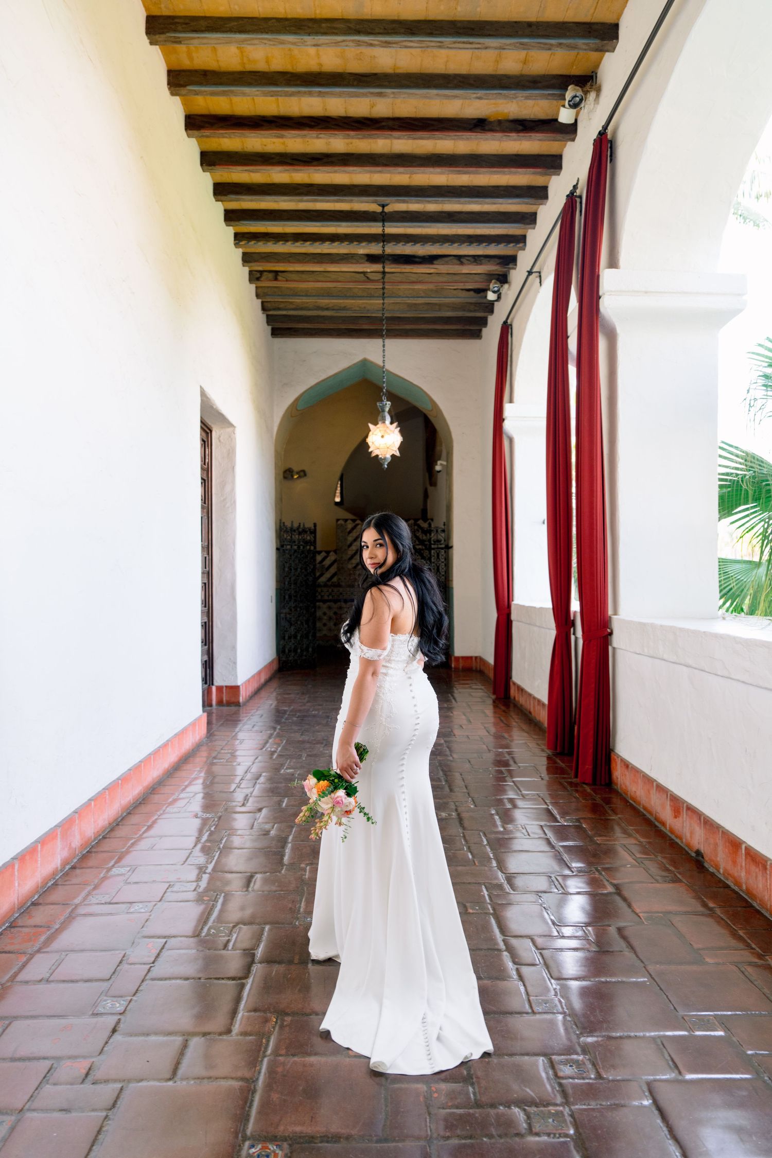 Interior corridor with Spanish colonial architecture featuring wooden beams and terra cotta floors.