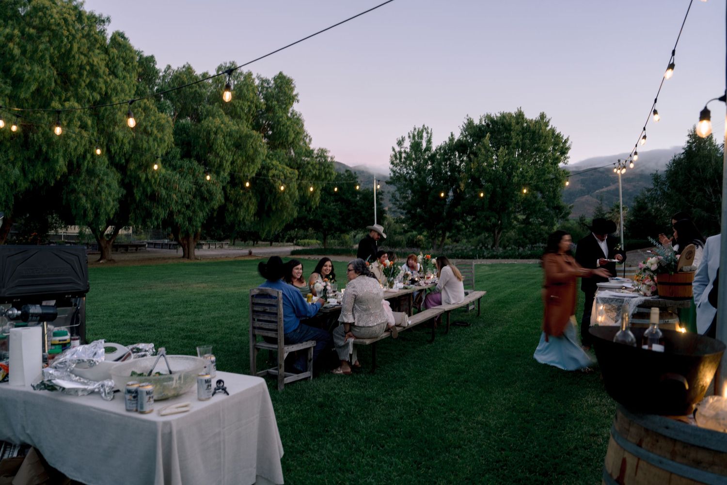 Outdoor wedding reception setup with string lights and tables at dusk.