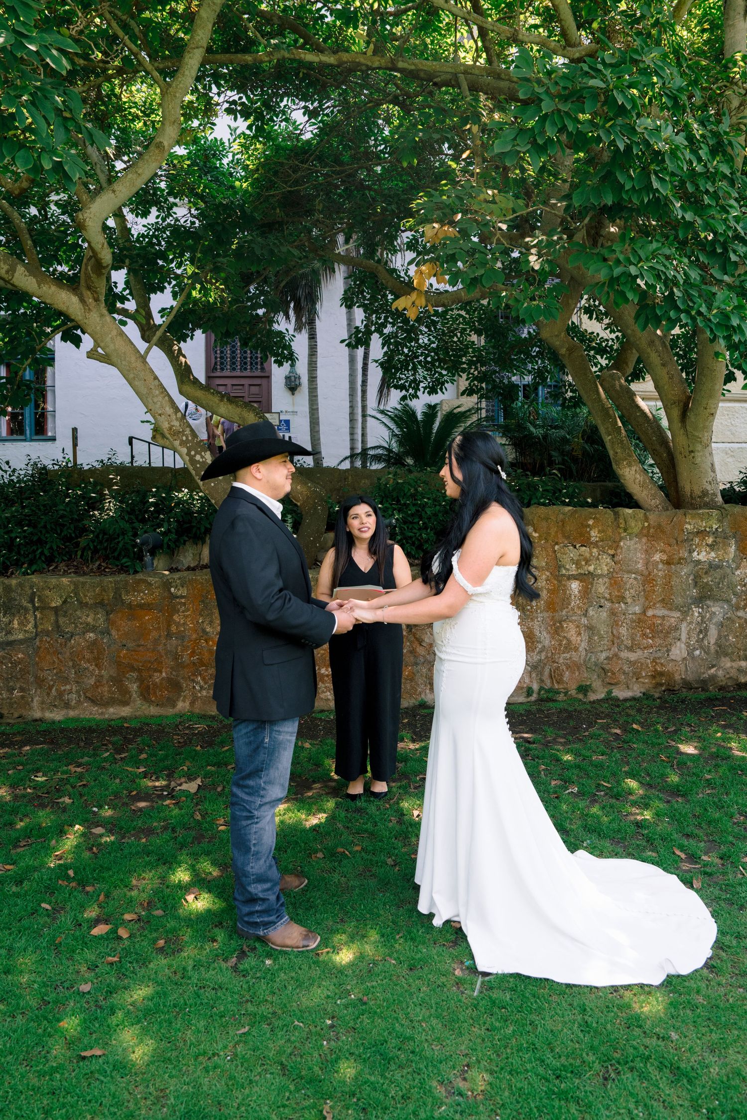 Wedding party poses for photos in a lush garden with stone wall backdrop.