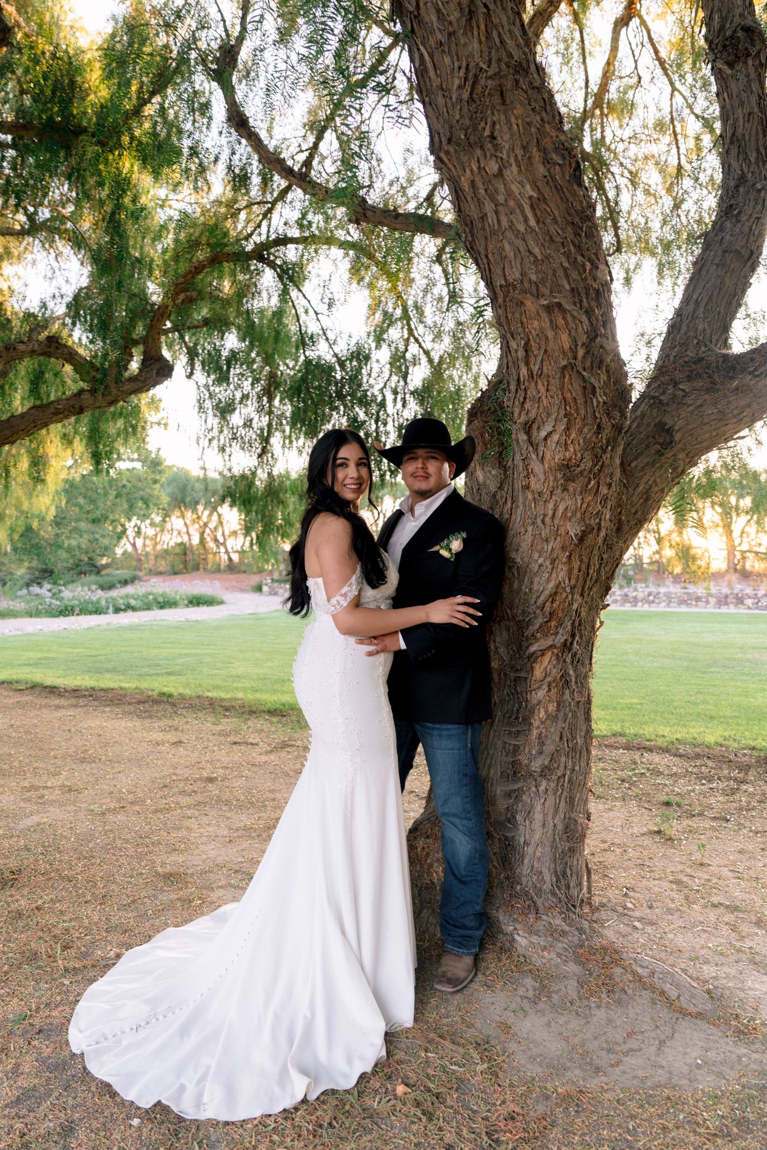 A newlywed couple poses under a large tree during their western-themed wedding.