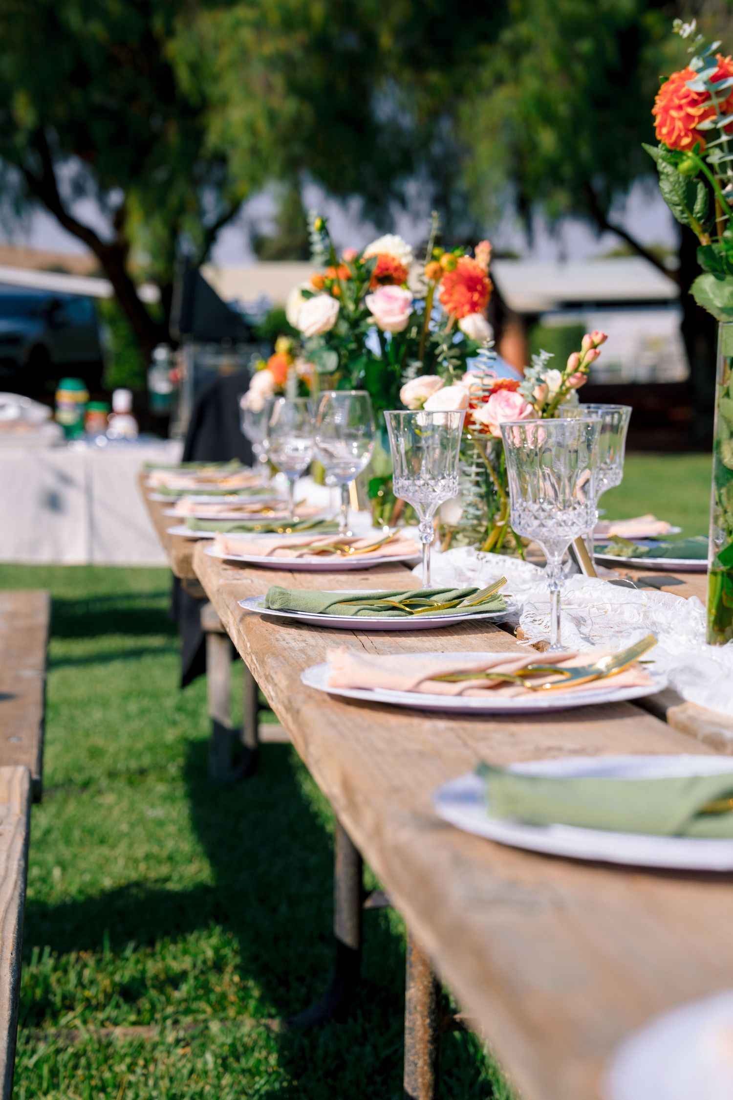 Elegant outdoor wedding table setting with white linens, place settings and floral centerpieces on a grassy lawn.