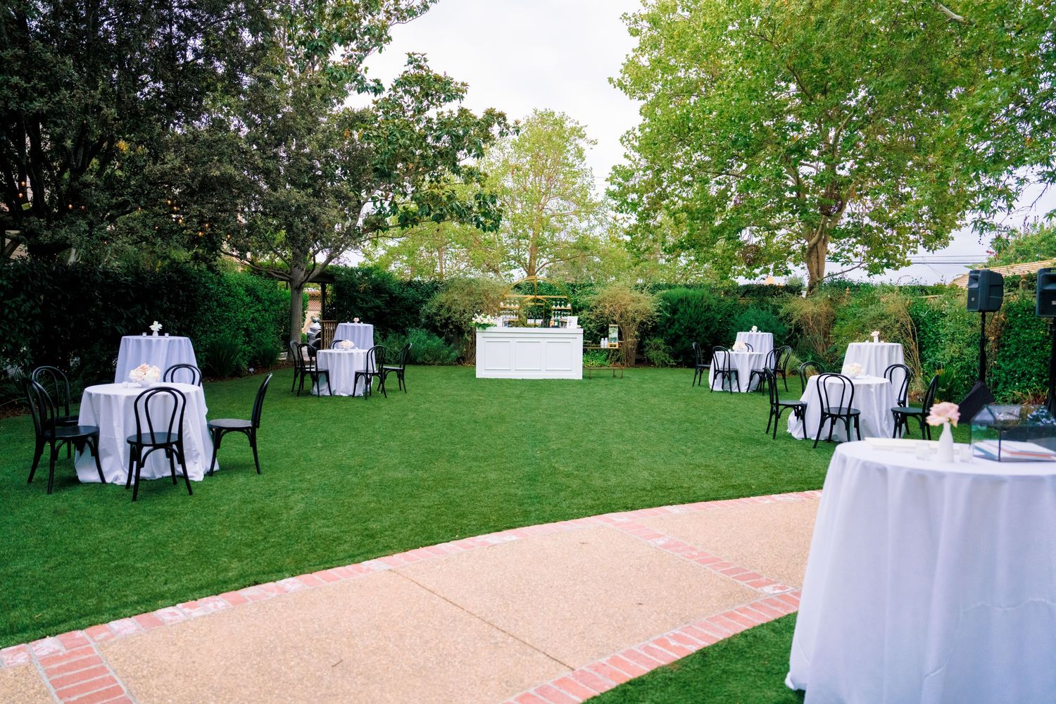 Outdoor wedding reception setup with round tables and white linens on a manicured lawn.