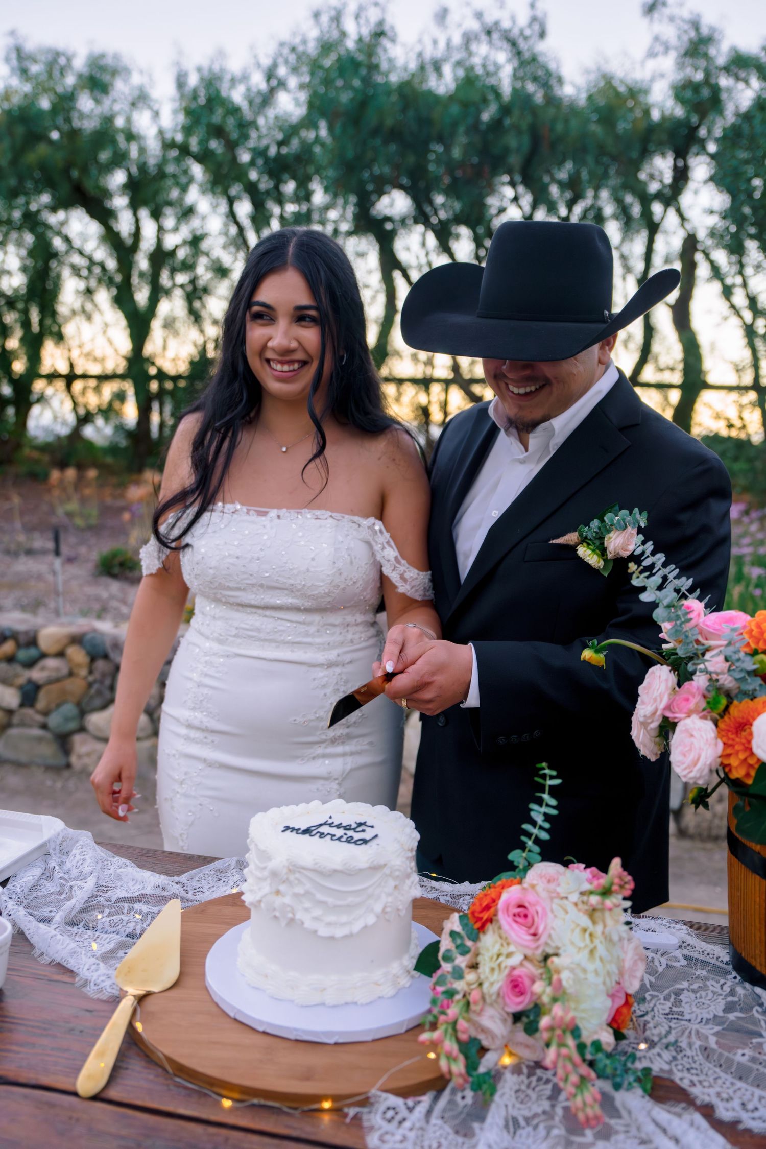 Couple cutting their wedding cake together at an outdoor reception with floral decorations.