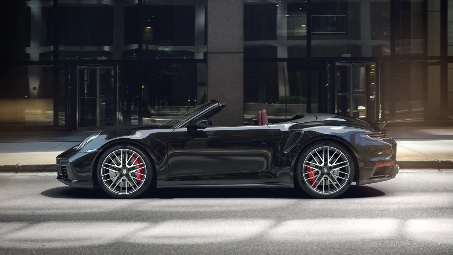 A black Porsche 911 Turbo convertible with red brake calipers parked on a city street at night.