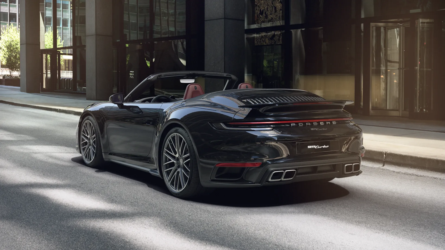 A sleek black Porsche 911 Turbo cabriolet parked on a city street at night with illuminated buildings in the background.
