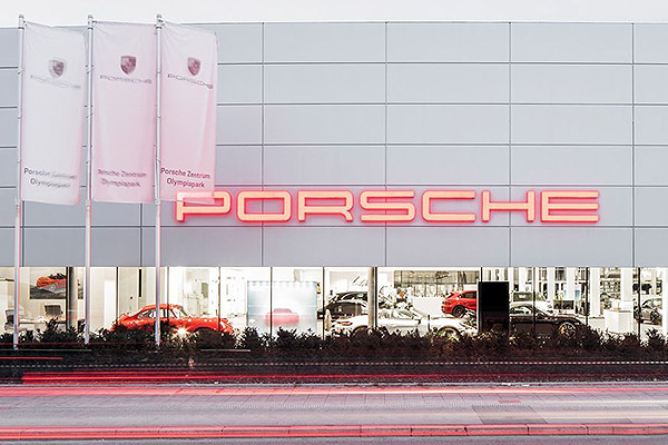 Sleek red Porsche dealership showroom exterior with large glass windows displaying luxury vehicles inside.