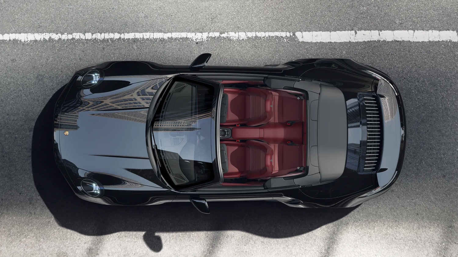 Sleek black Porsche 911 Turbo convertible with red interior viewed from above on gray pavement.