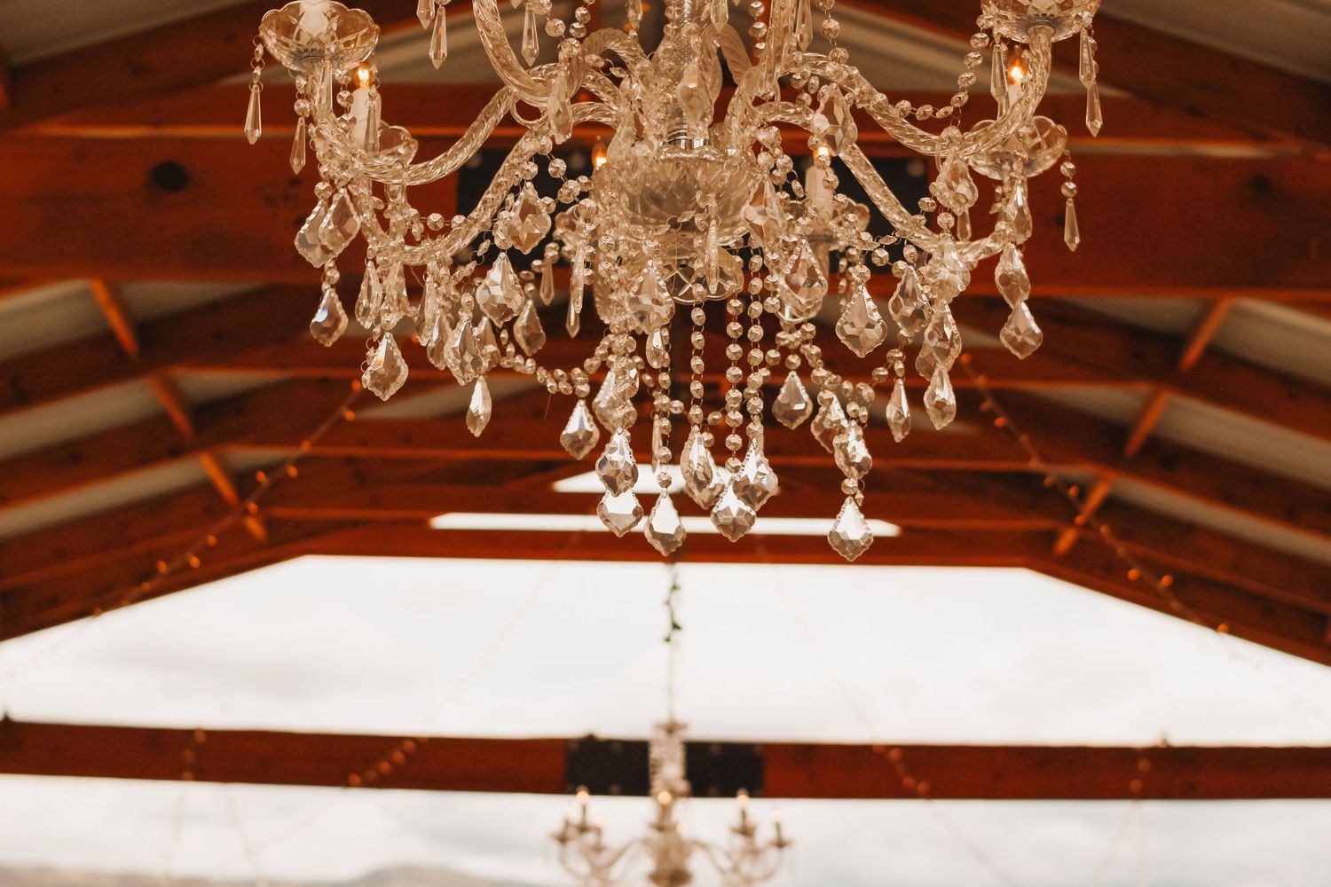 Elegant crystal chandelier hanging from wooden beamed ceiling at wedding venue.
