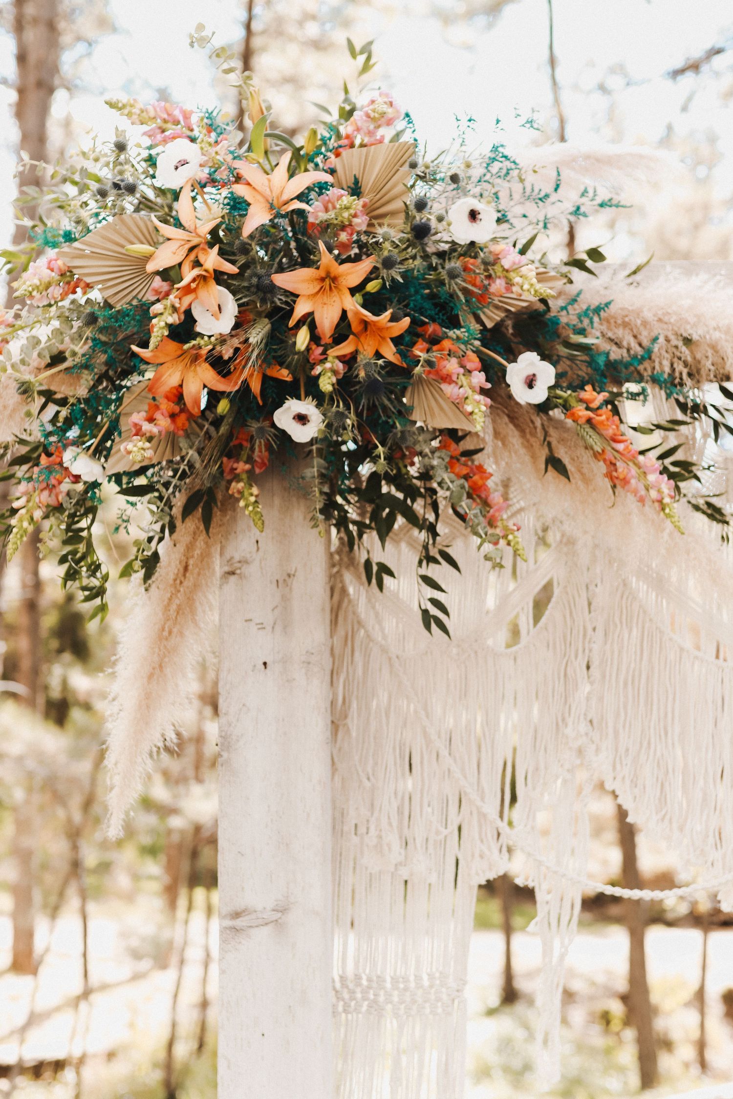 White macrame backdrop decorated with orange and white floral arrangements for wedding ceremony.