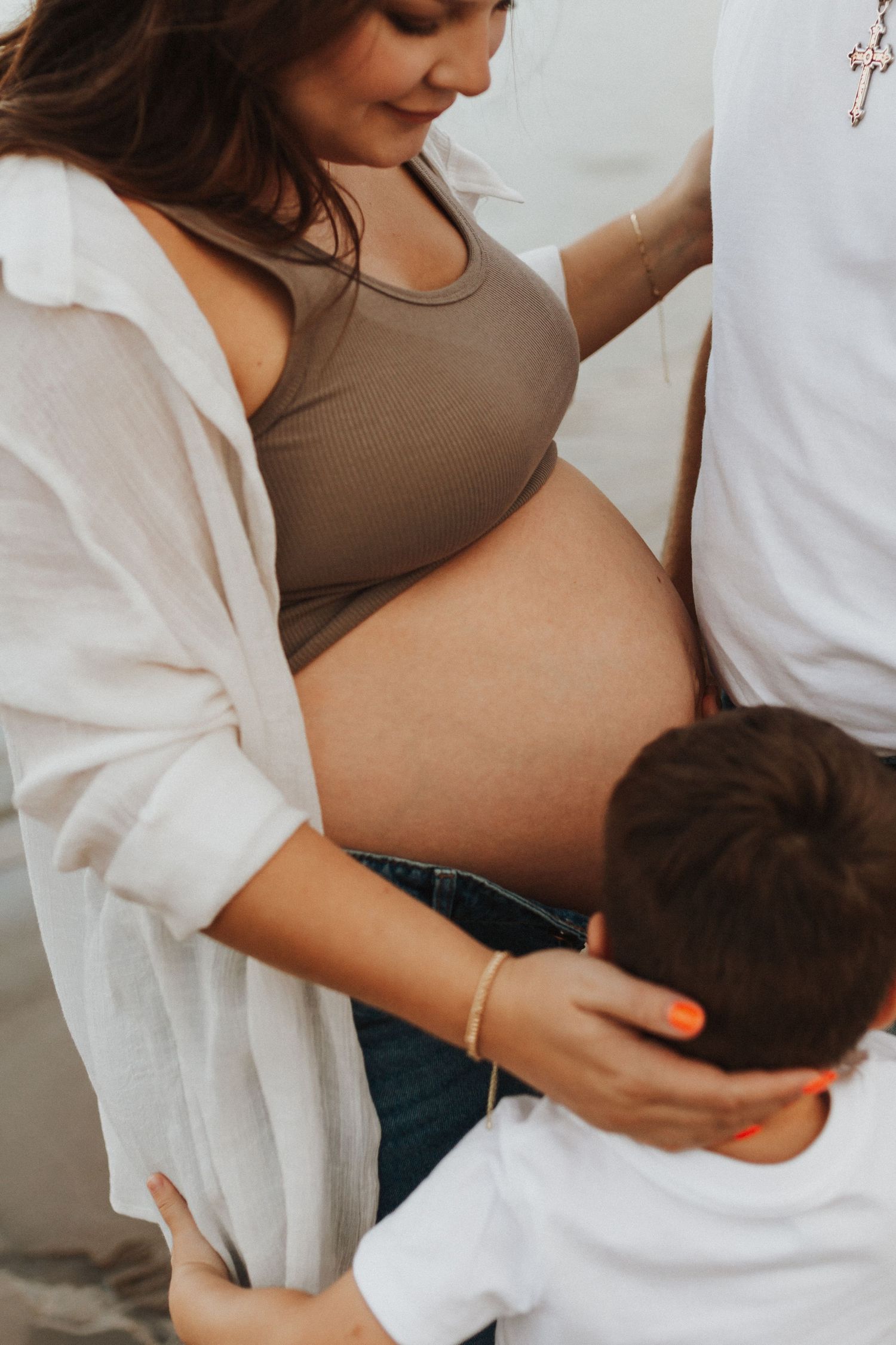 Intimate maternity moment showing a pregnant belly and white cardigan.