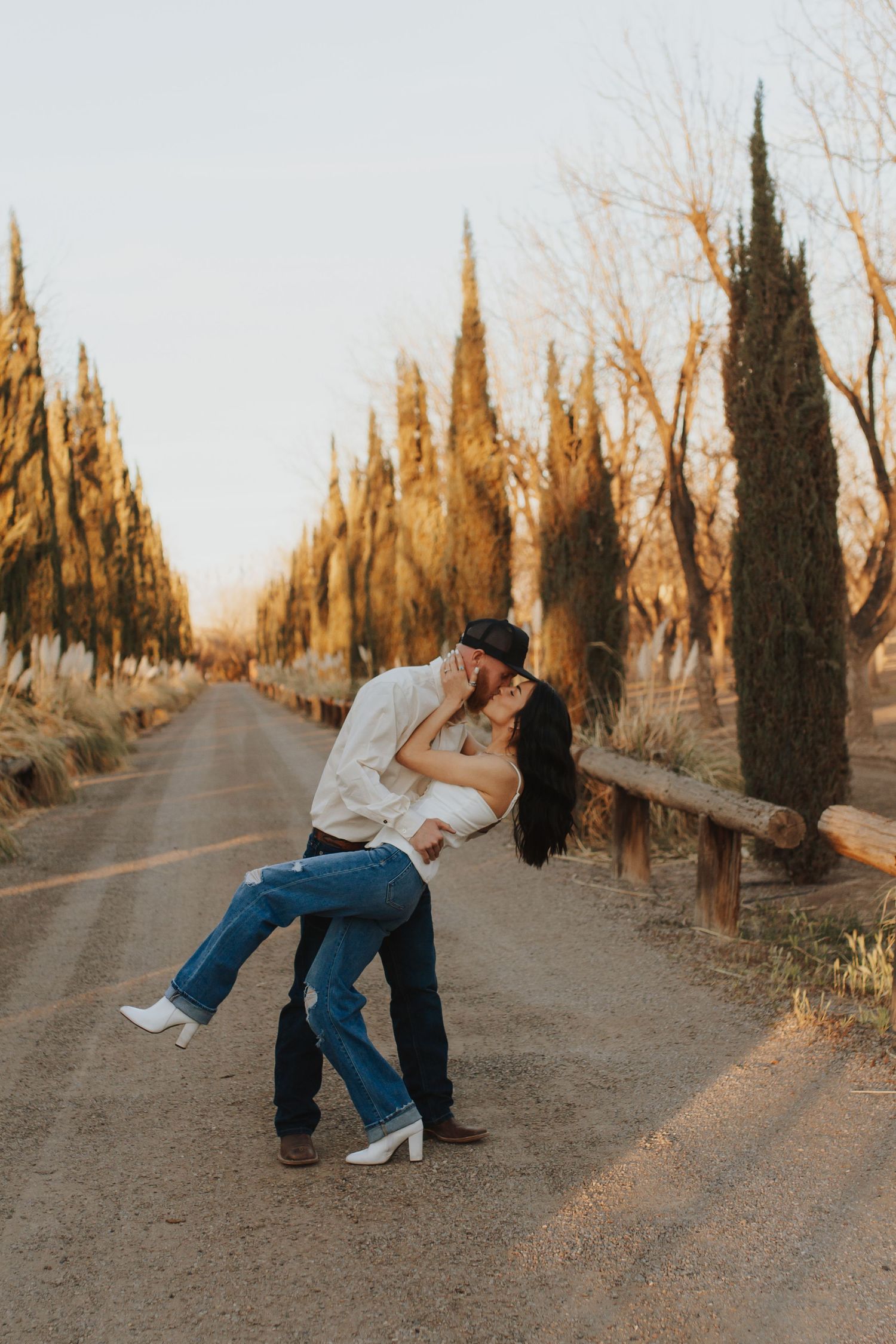 A romantic couple dances together on a cypress tree-lined path at golden hour.