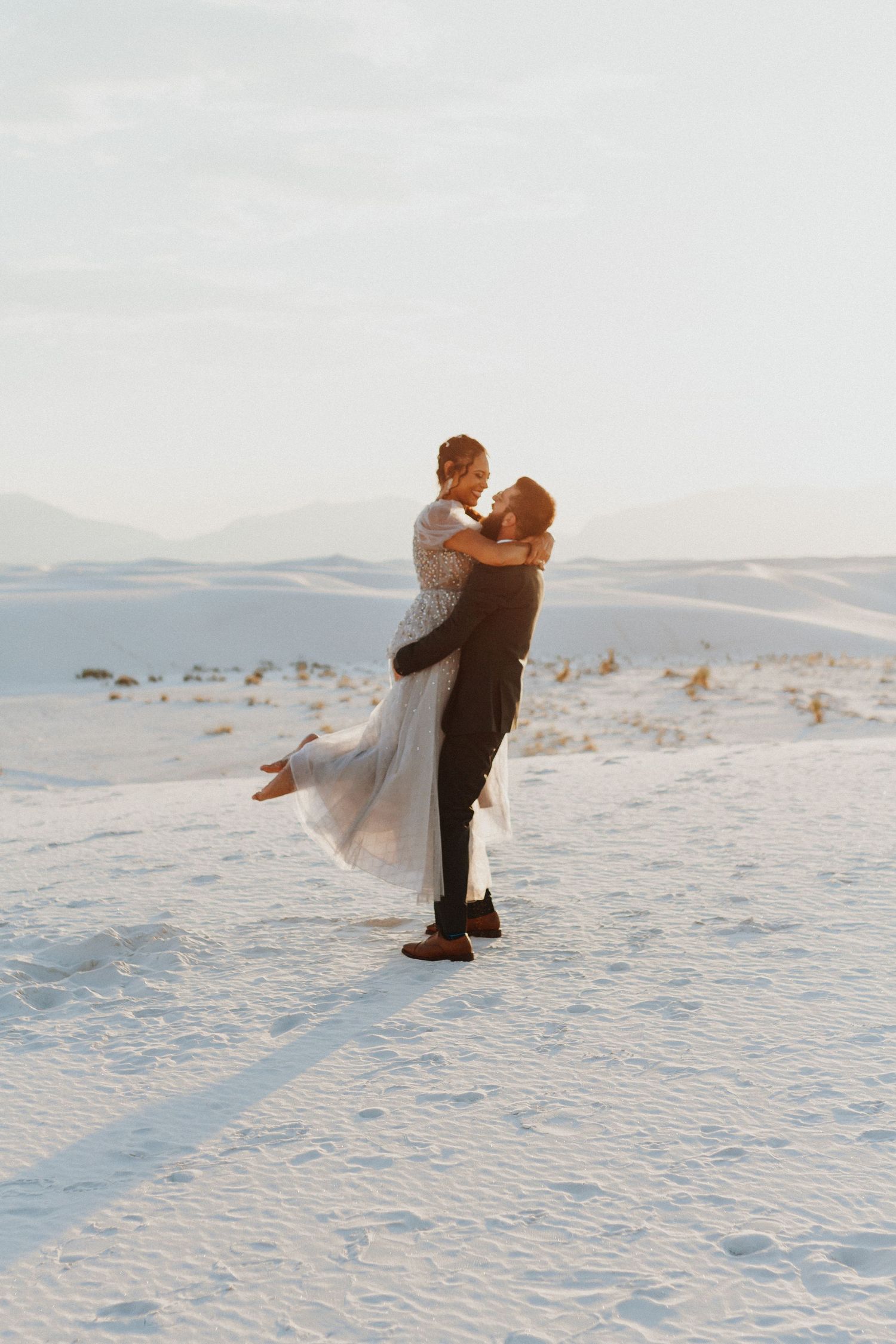 Romantic winter wedding photo of couple embracing in white snow landscape.